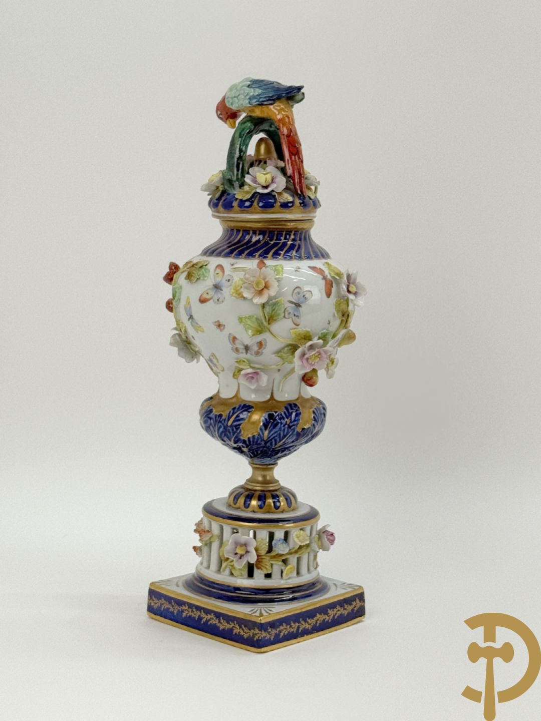 Porseleinen siervaas met handbeschilderd geanimeerd decor bezet met basrelief van bloemen en bovenaan bekroond met deksel met vogel