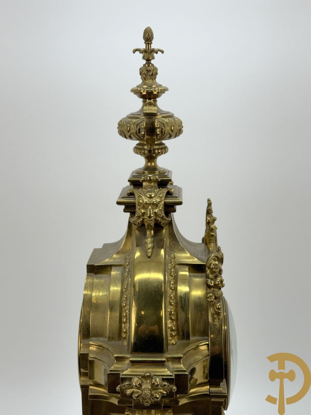 Vuurvergulde bronzen pendule, zijdelings bezet met gevleugelde dames, bovenaan met amfoor