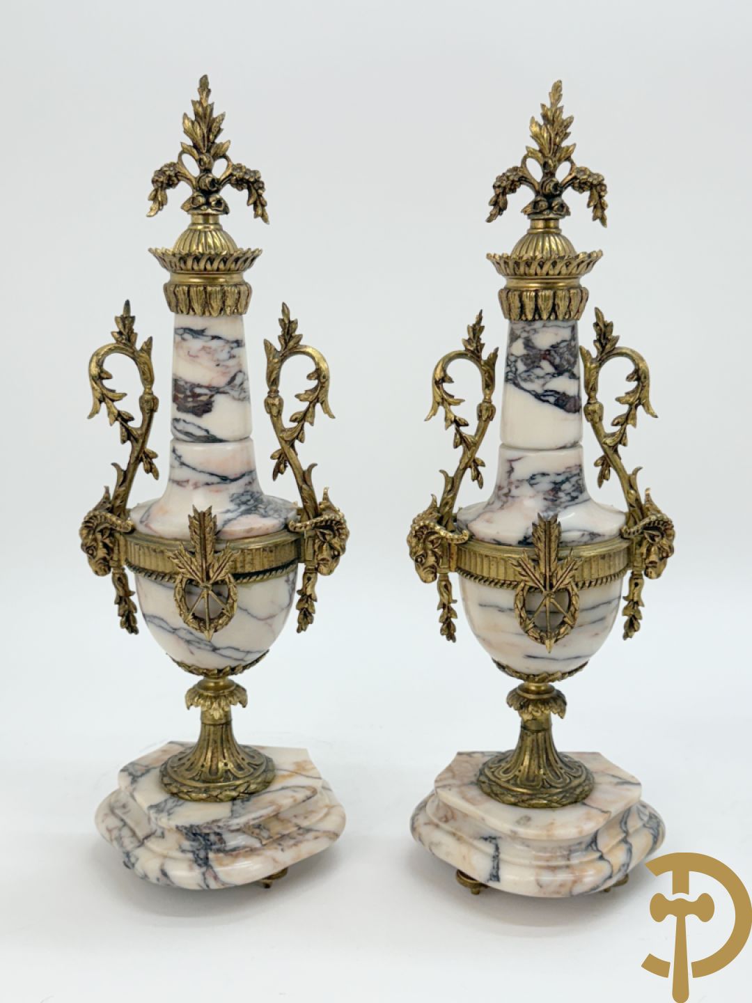 Driedelige wit marmeren garnituur bestaande uit vierzuilenpendule met bloemen en troffee geflankeerd door paar cassolettes met ramskoppen bezet