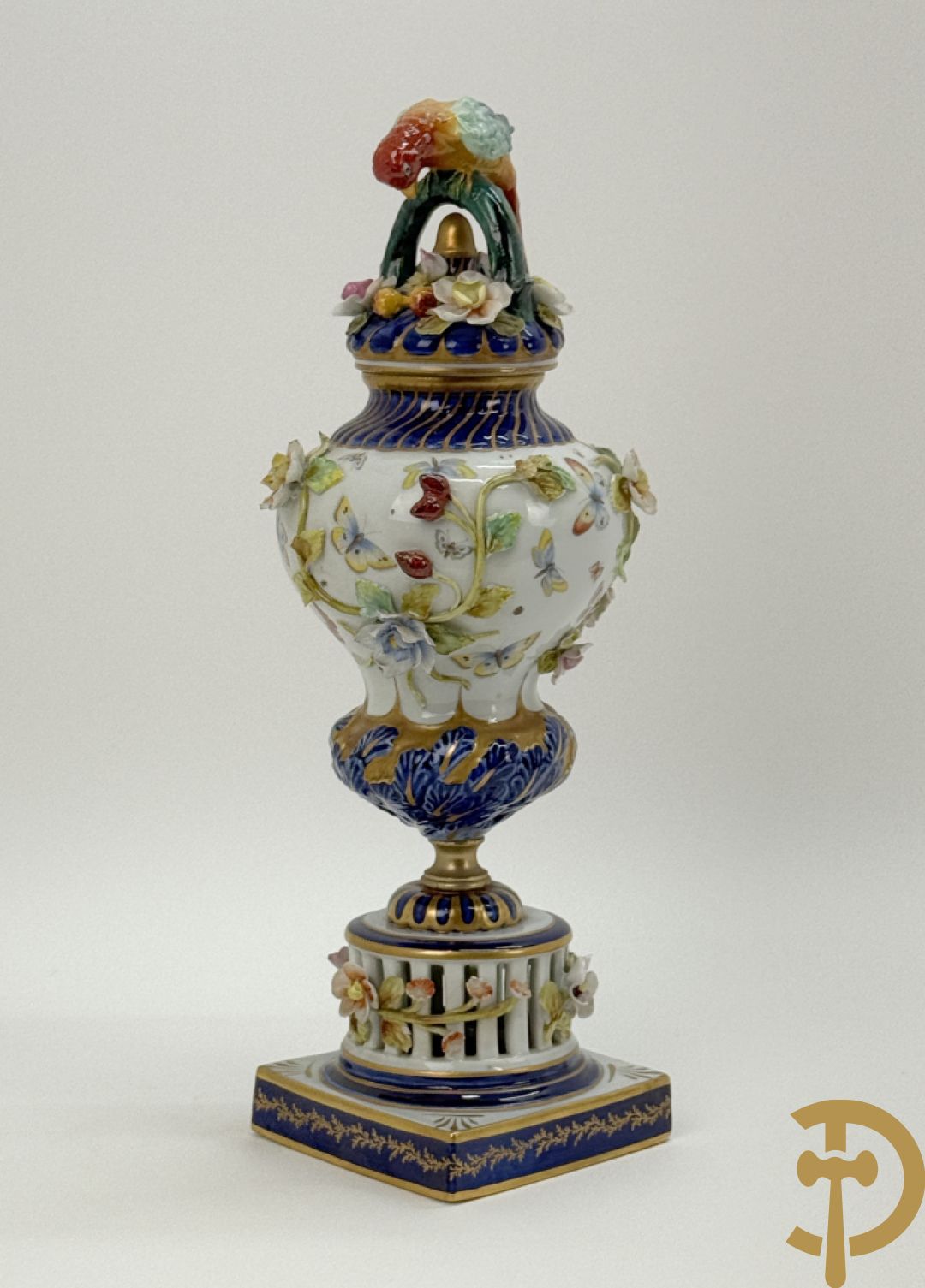 Porseleinen siervaas met handbeschilderd geanimeerd decor bezet met basrelief van bloemen en bovenaan bekroond met deksel met vogel