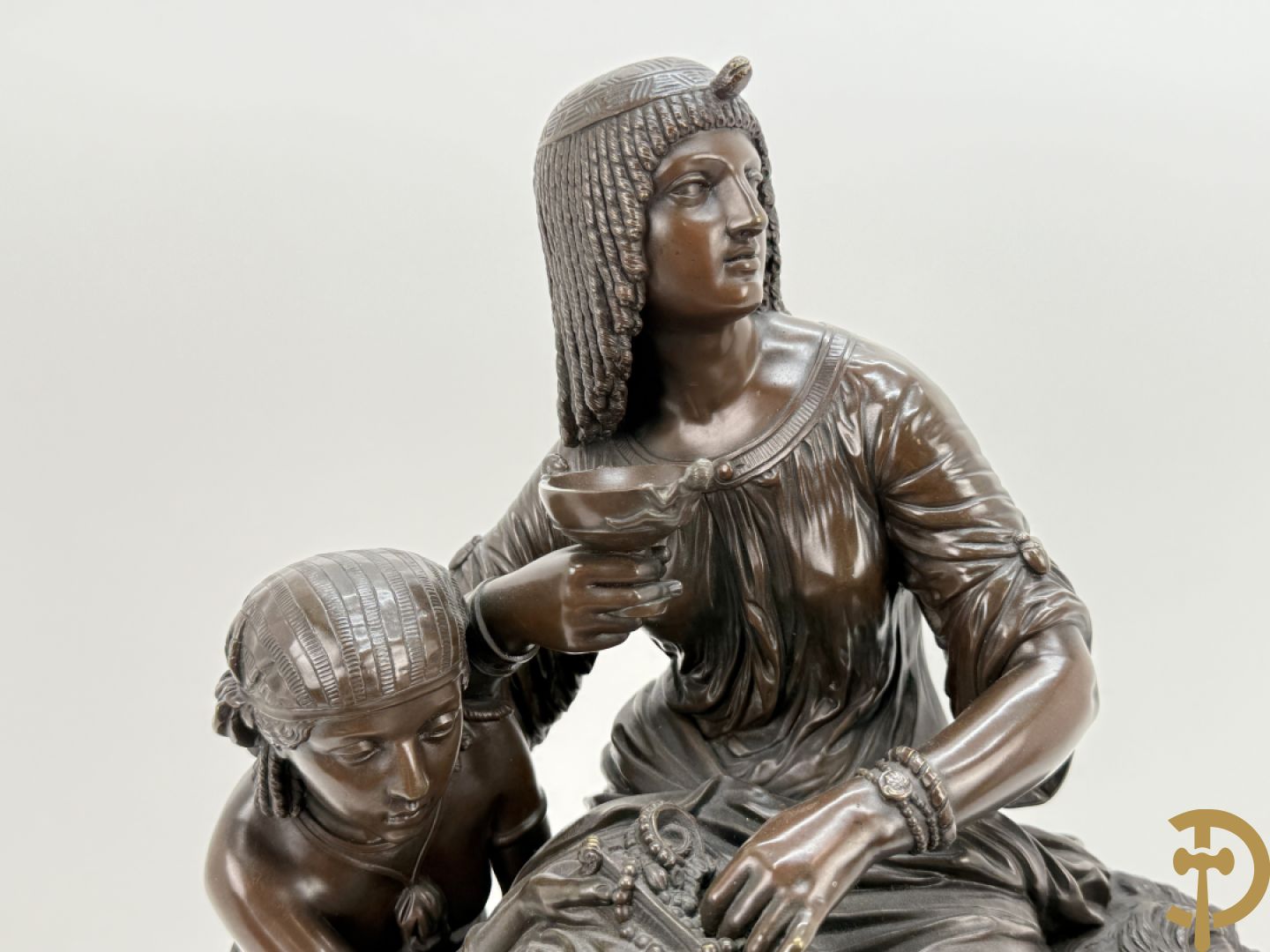 Driedelige bronzen garnituur bestaande uit middenstuk met bronzen vuurvergulde klok, Daubrée gemerkt à Nancy, bovenaan bekroond met Cleopatra met drinkbeker - getekend van Cumberworth sculpteur - geflankeerd door paar cupido