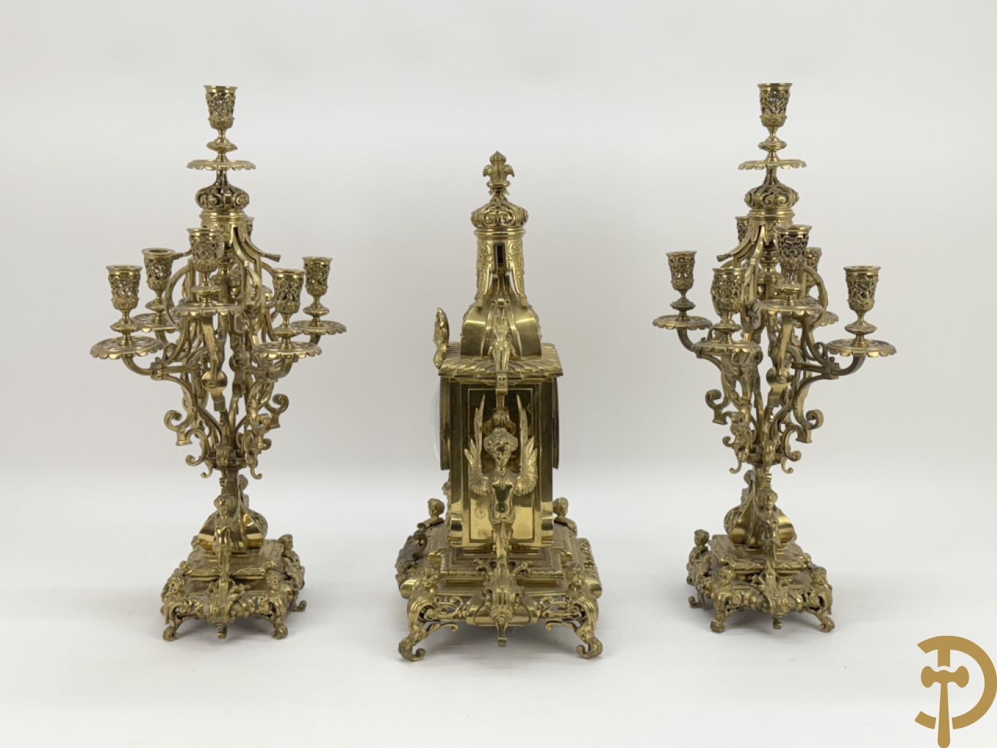 Driedelige bronzen vergulde garntiuur bestaande uit klok met medusahoofden en sfinxen, geflankeerd door paar zevenarmige kandelaars met accanthusranken en sfinxen