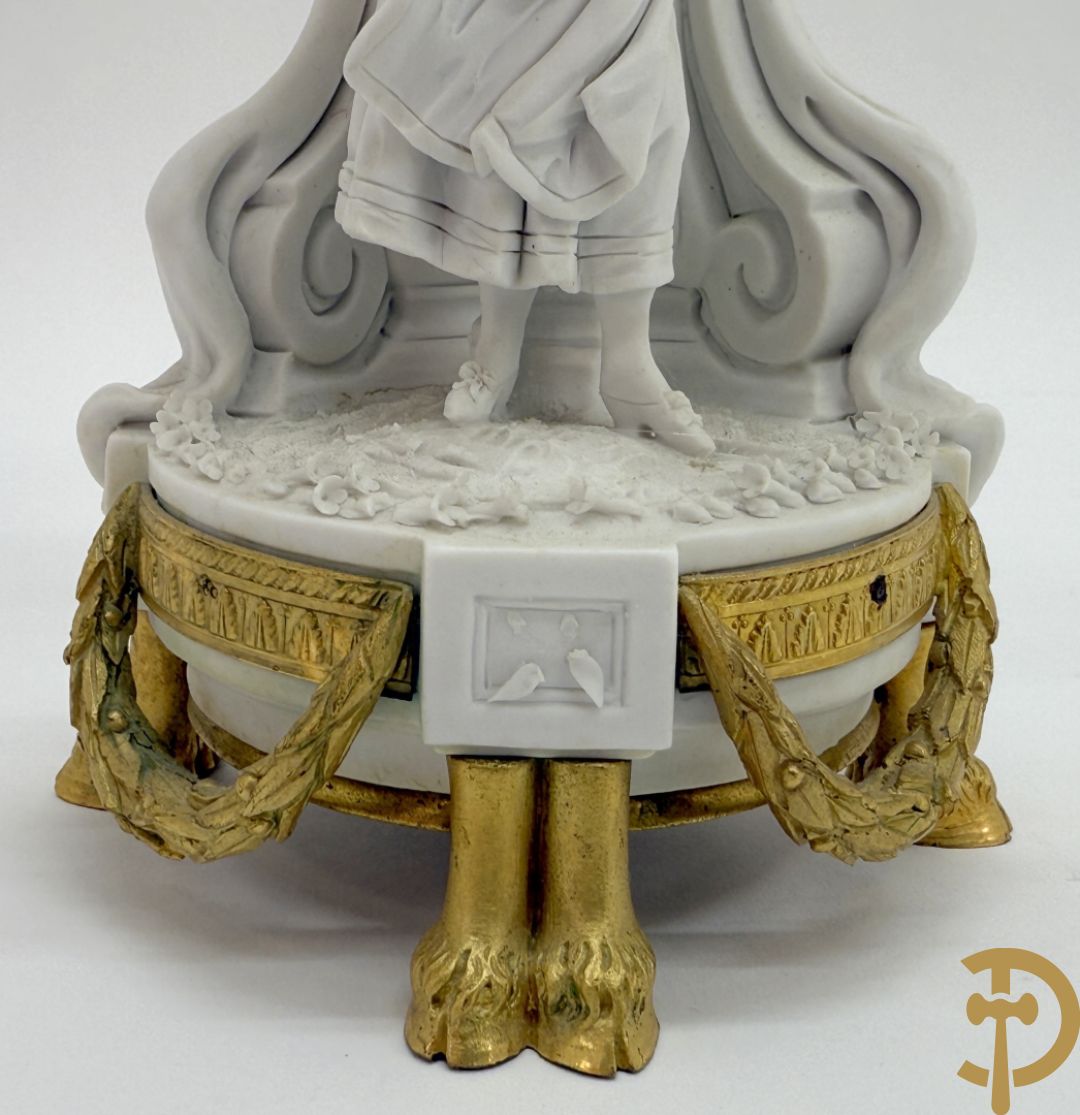 Driedelige porseleinen garnituur met bronsbeslag bestaande uit pendule met dame en amfoor geflankeerd door paar kandelaars bezet met personages