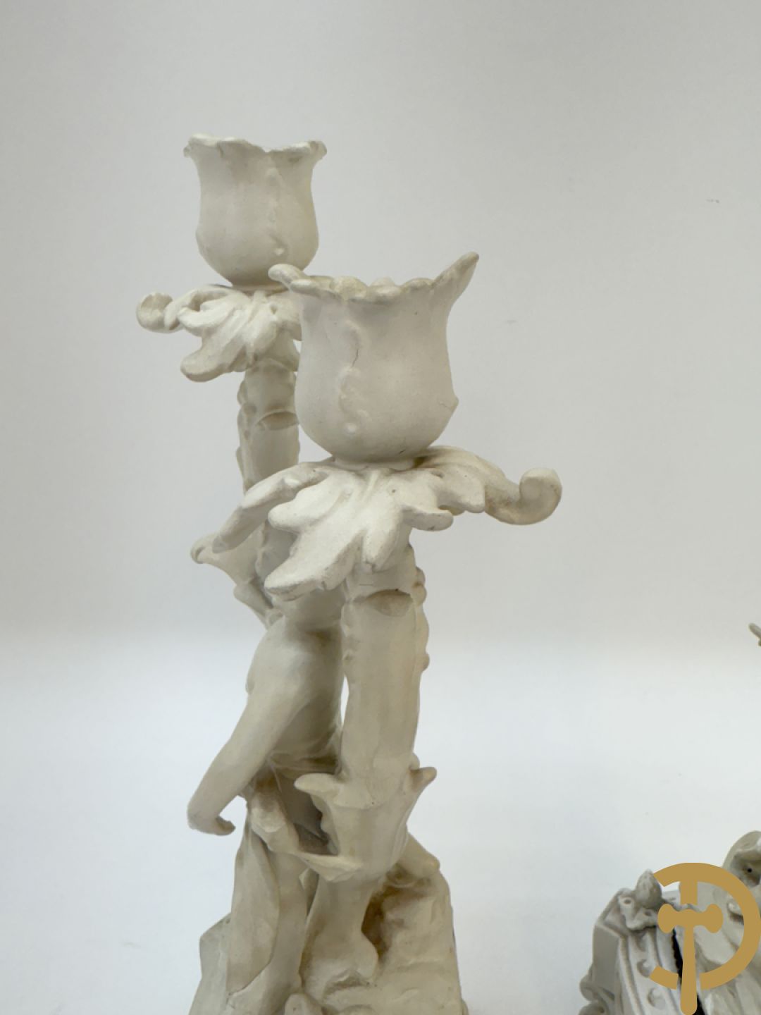 Driedelige porseleinen garnituur bestaande uit pendule bezet met lieftallig koppel, geflankeerd door paar kandelaars met cupido