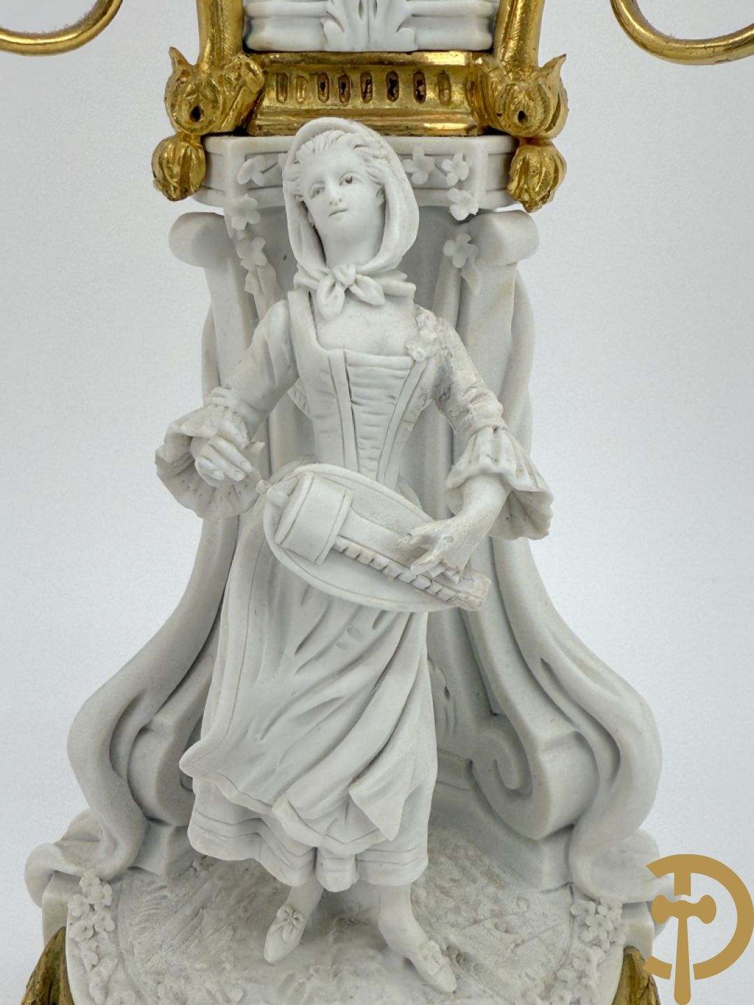 Driedelige porseleinen garnituur met bronsbeslag bestaande uit pendule met dame en amfoor geflankeerd door paar kandelaars bezet met personages