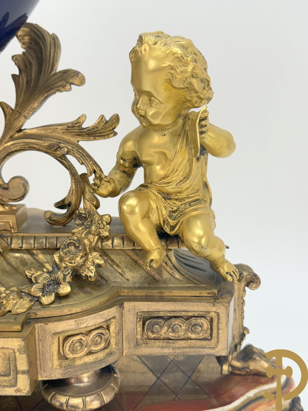 Driedelige vergulde bronzen garnituur bestaande uit pendule met blauw porseleinen coupe geflankeerd door 2 cupido