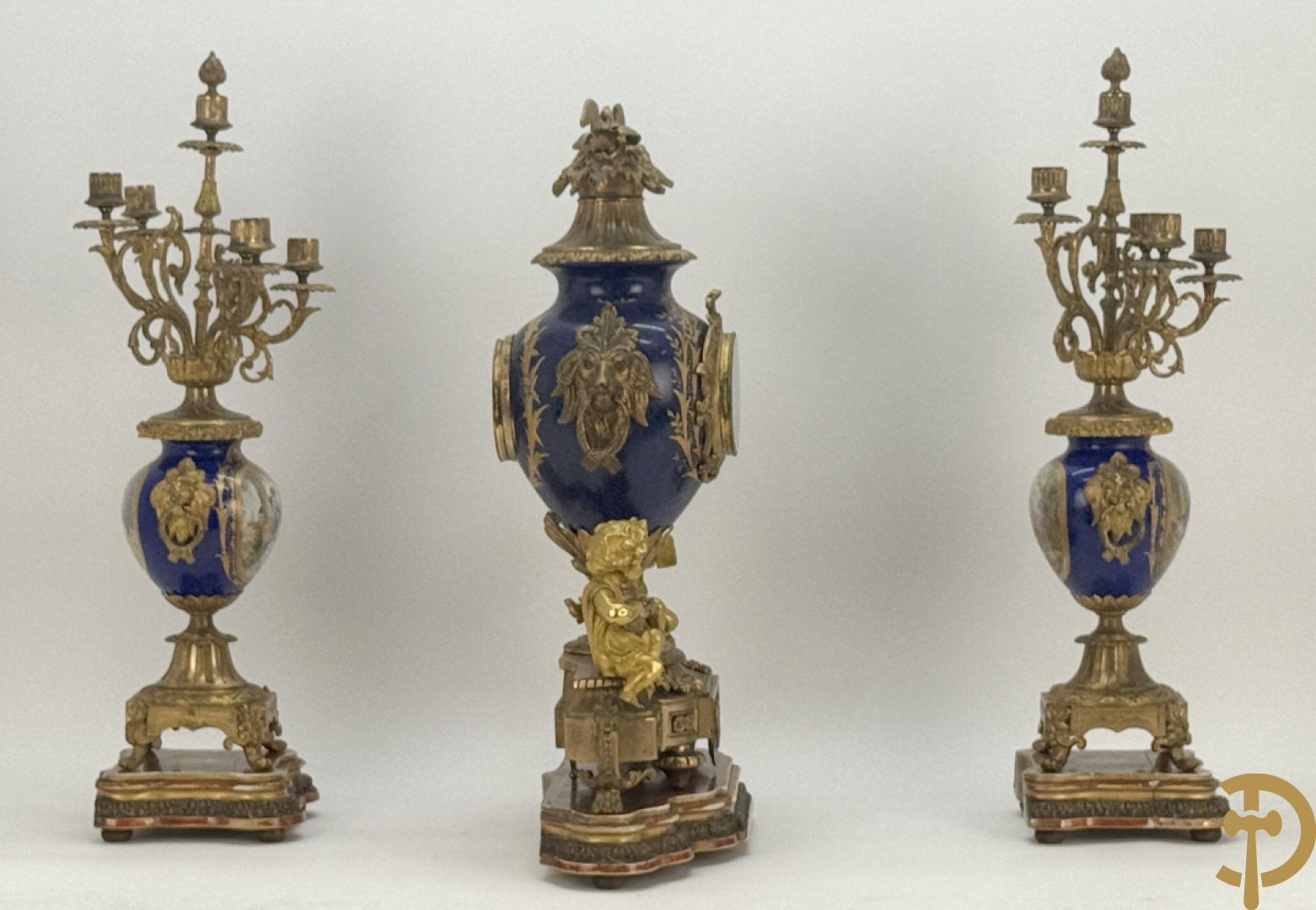 Driedelige vergulde bronzen garnituur bestaande uit pendule met blauw porseleinen coupe geflankeerd door 2 cupido