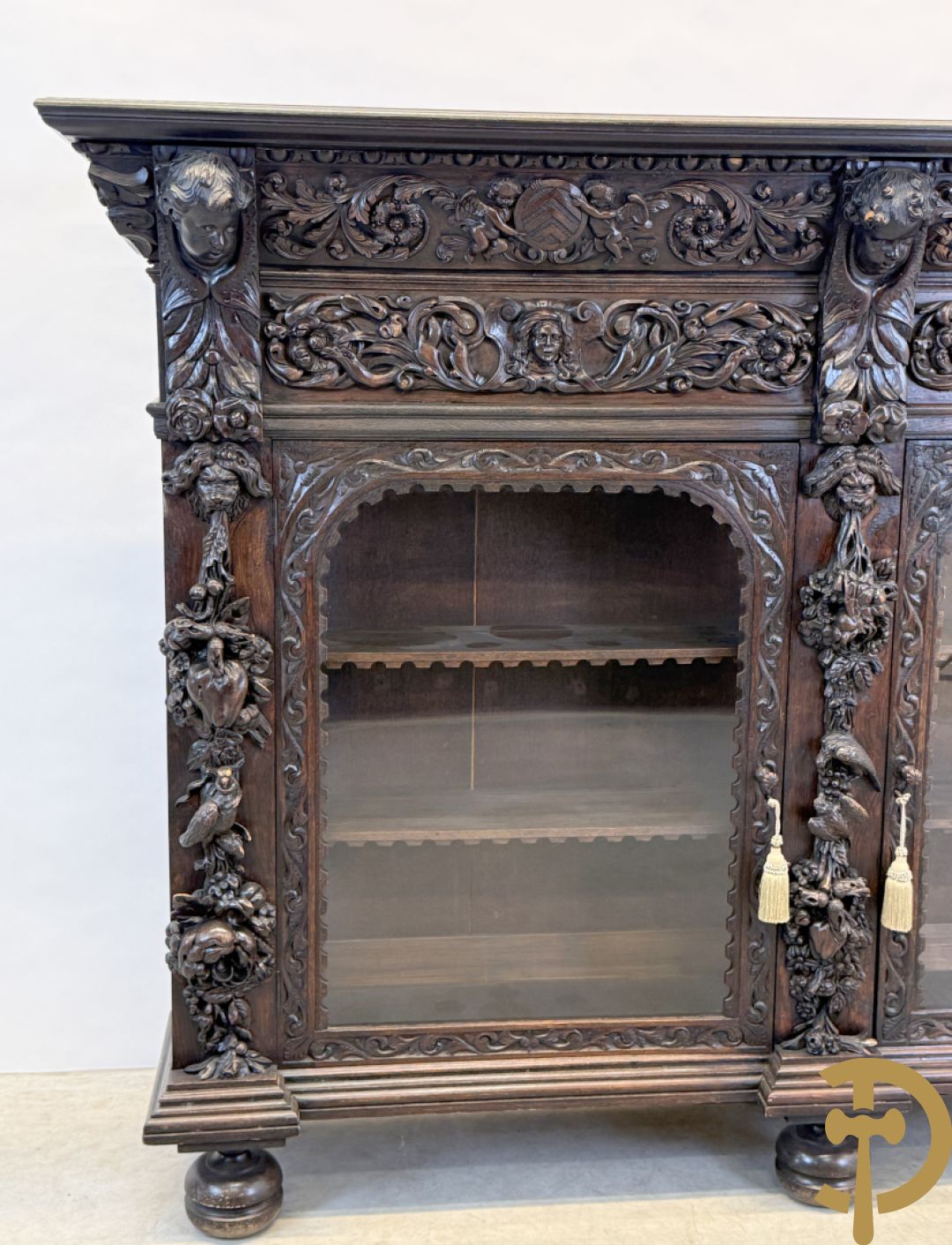 Tweedeursvitrine met Neo Renaissance sculptuur, bovenaan mlet cupidohoofden, bloemen en accanthusranken