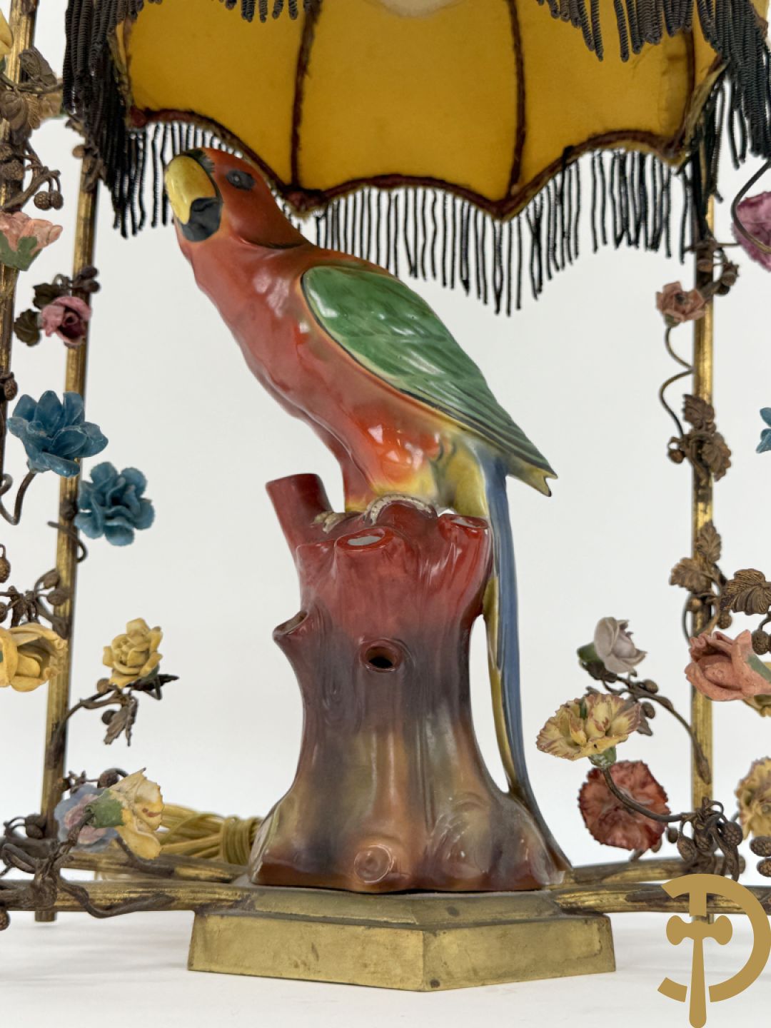 Handgekleurde porseleinen papegaai onder koperen boog met bloemen bezet, als lampadaire