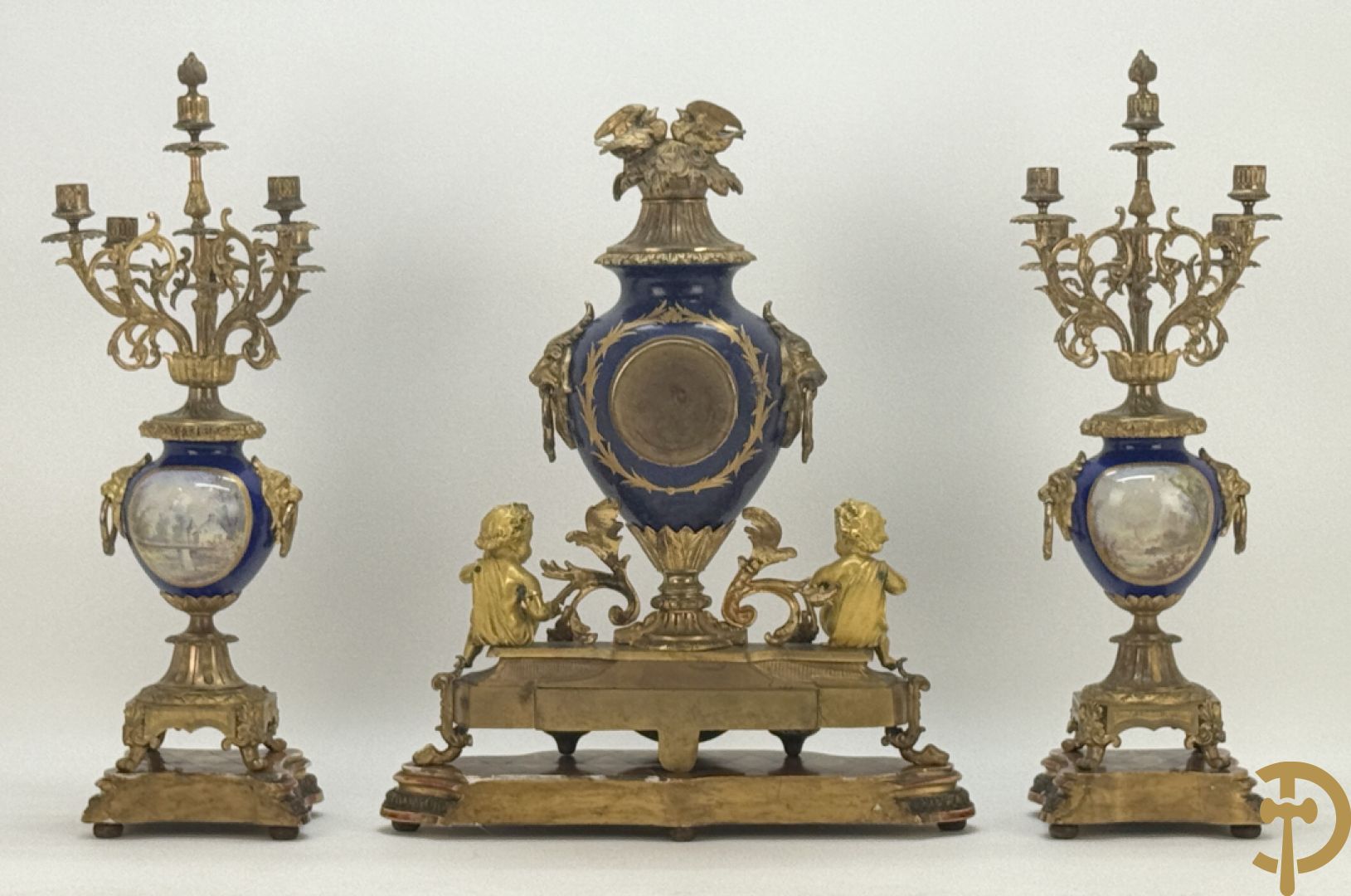 Driedelige vergulde bronzen garnituur bestaande uit pendule met blauw porseleinen coupe geflankeerd door 2 cupido