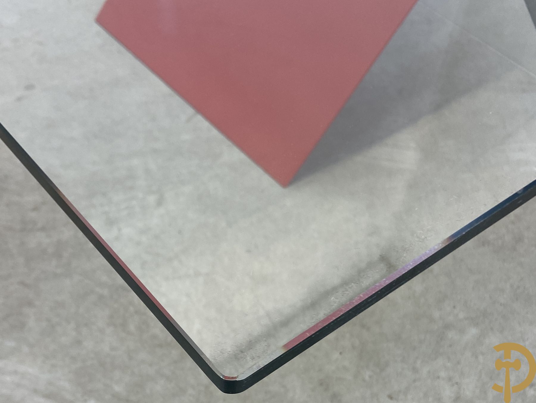 Design salontafel met glazen gepolijst blad op rood gelakte driehoekig prisma sokkel