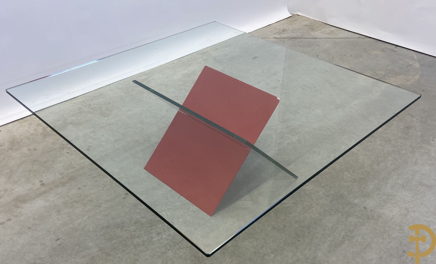 Design salontafel met glazen gepolijst blad op rood gelakte driehoekig prisma sokkel