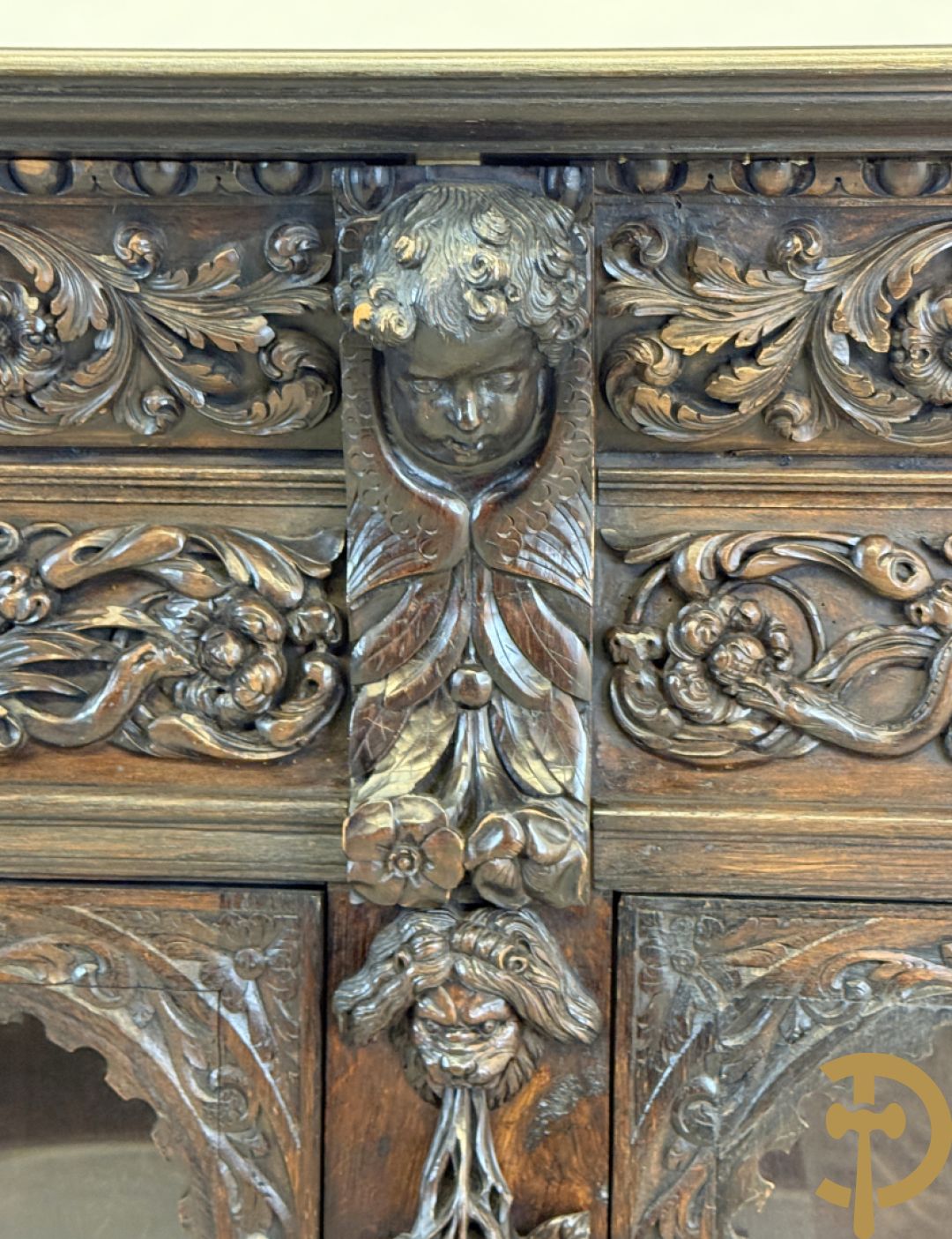 Tweedeursvitrine met Neo Renaissance sculptuur, bovenaan mlet cupidohoofden, bloemen en accanthusranken
