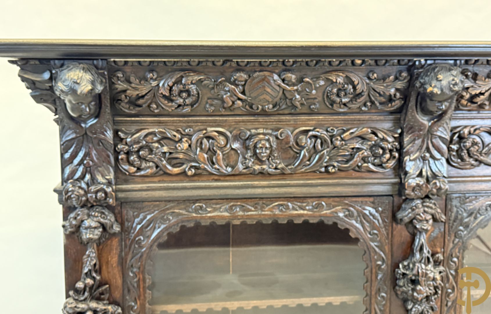 Tweedeursvitrine met Neo Renaissance sculptuur, bovenaan mlet cupidohoofden, bloemen en accanthusranken