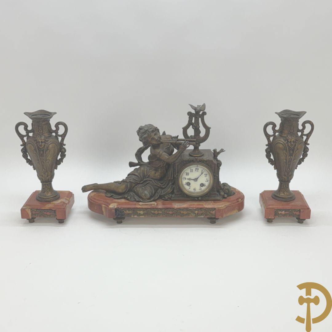 Driedelige garnituur, centraal horloge gedecoreerd met zamak beeld van fluitspelende cupido, geflankeerd door paar cassolettes - alles op marmeren basis