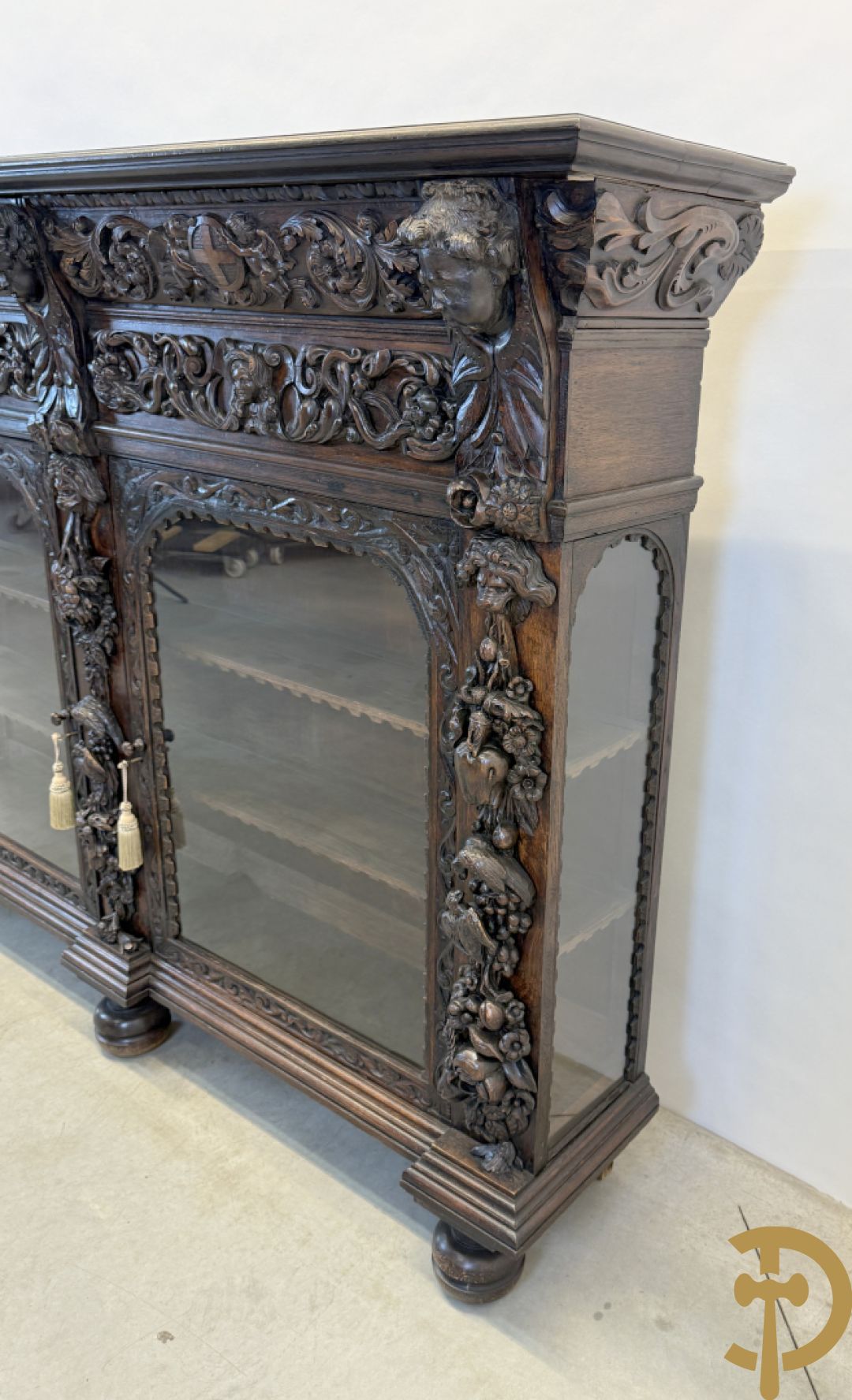Tweedeursvitrine met Neo Renaissance sculptuur, bovenaan mlet cupidohoofden, bloemen en accanthusranken