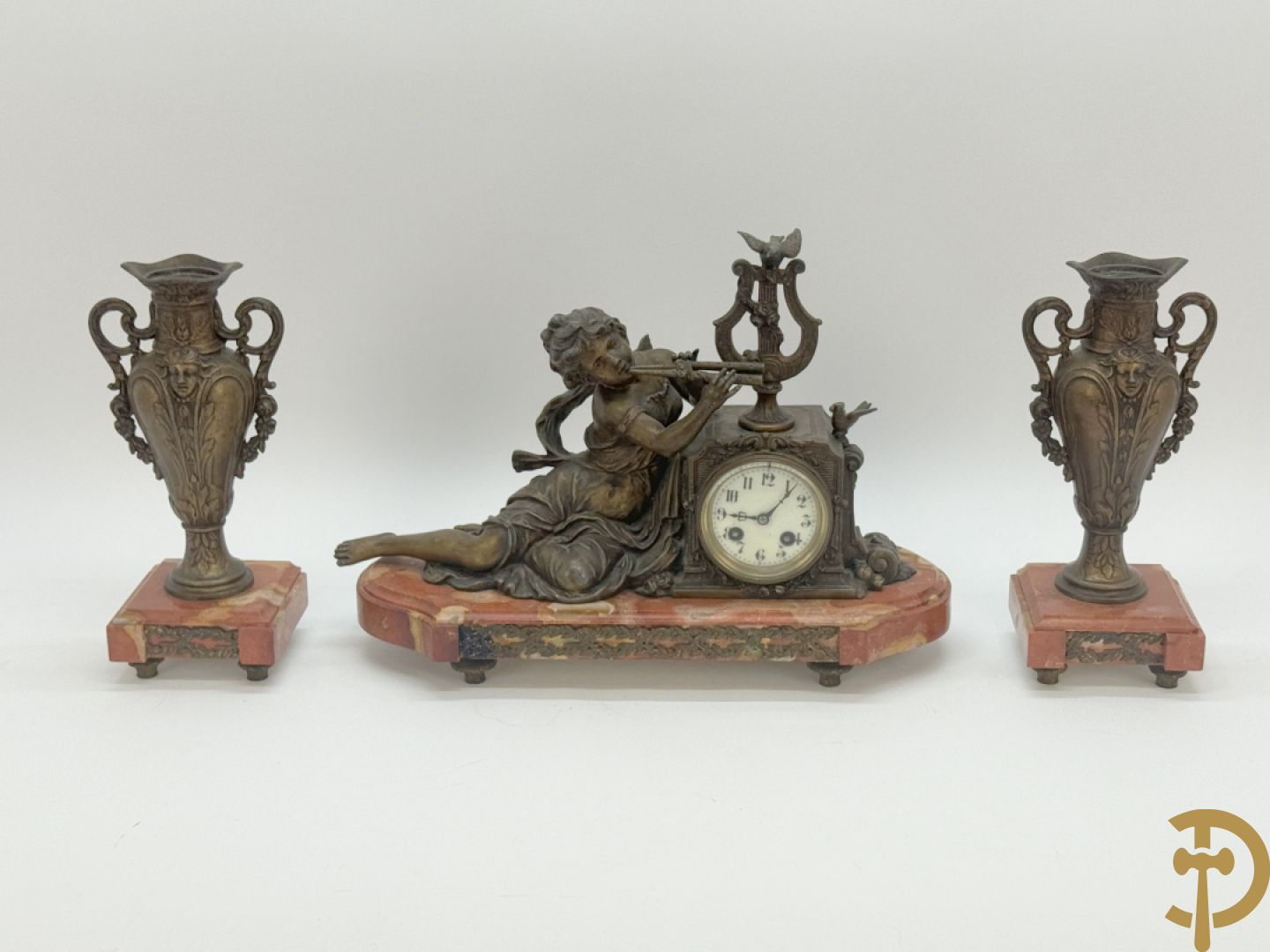 Driedelige garnituur, centraal horloge gedecoreerd met zamak beeld van fluitspelende cupido, geflankeerd door paar cassolettes - alles op marmeren basis