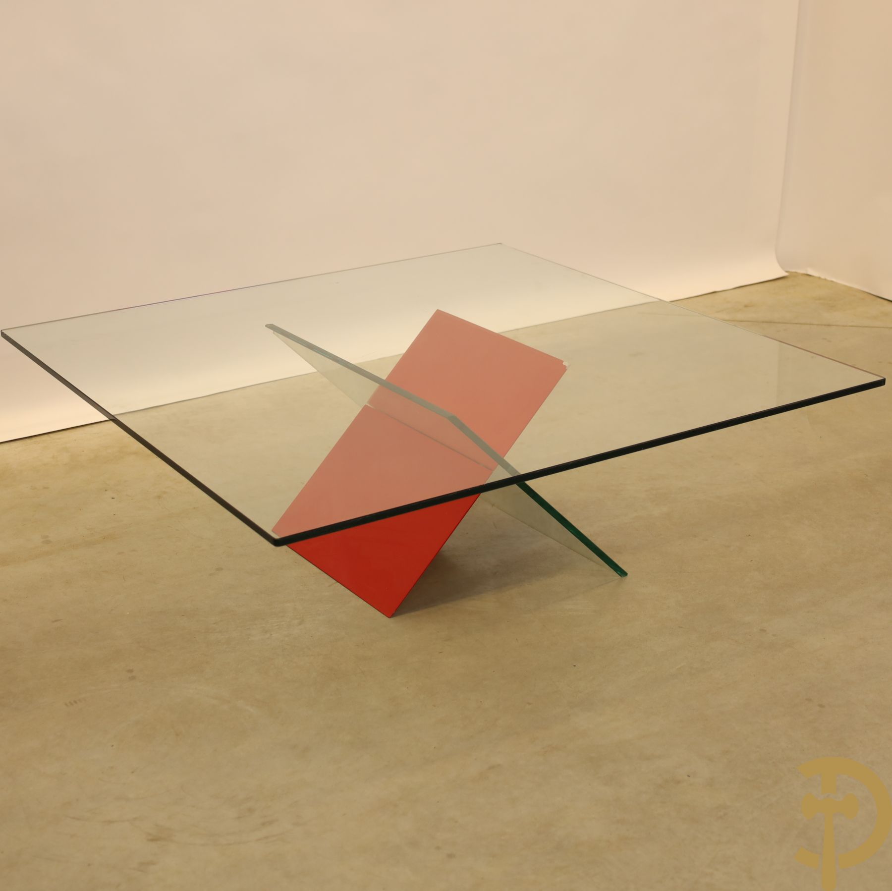Design salontafel met glazen gepolijst blad op rood gelakte driehoekig prisma sokkel