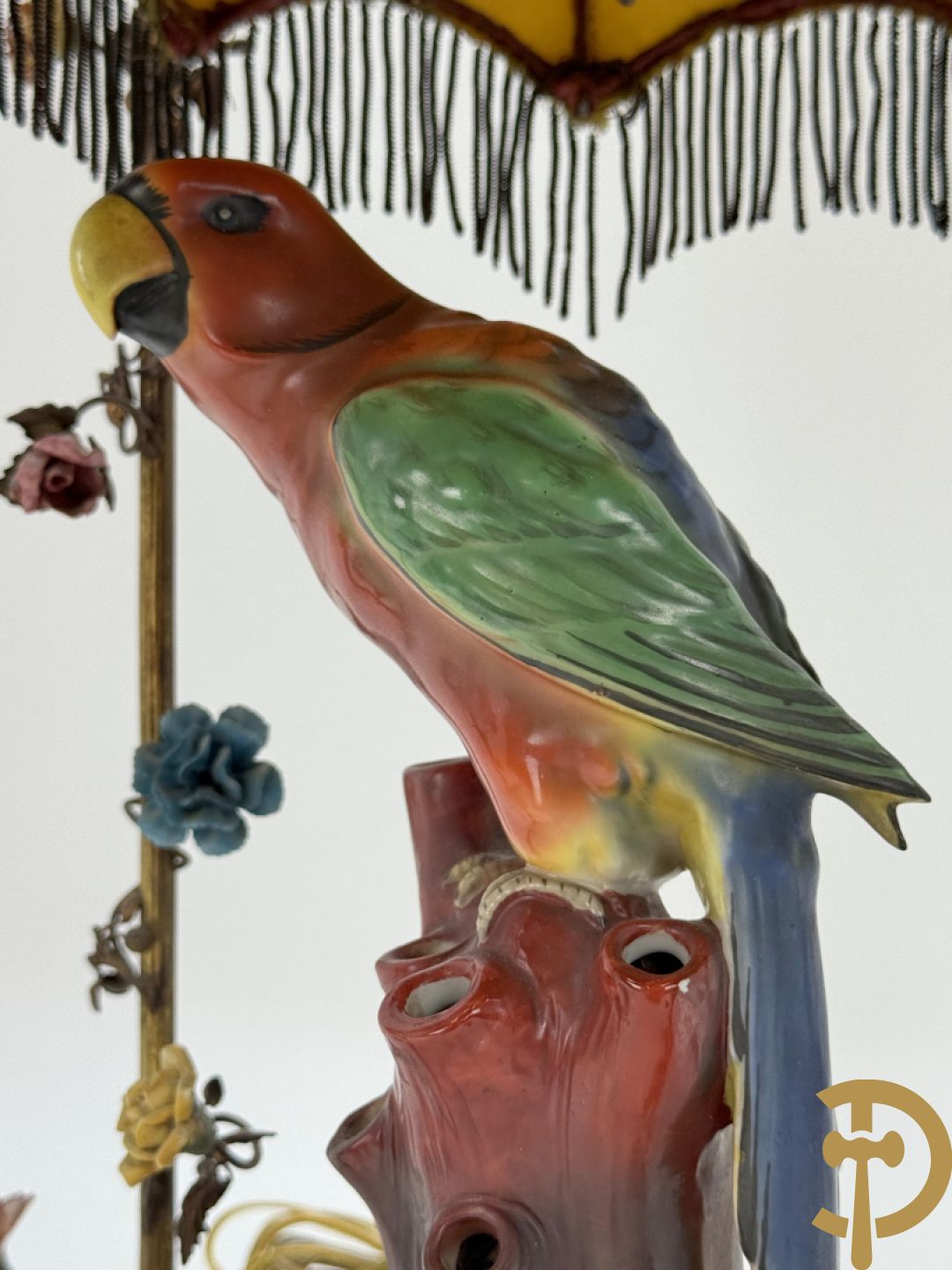 Handgekleurde porseleinen papegaai onder koperen boog met bloemen bezet, als lampadaire