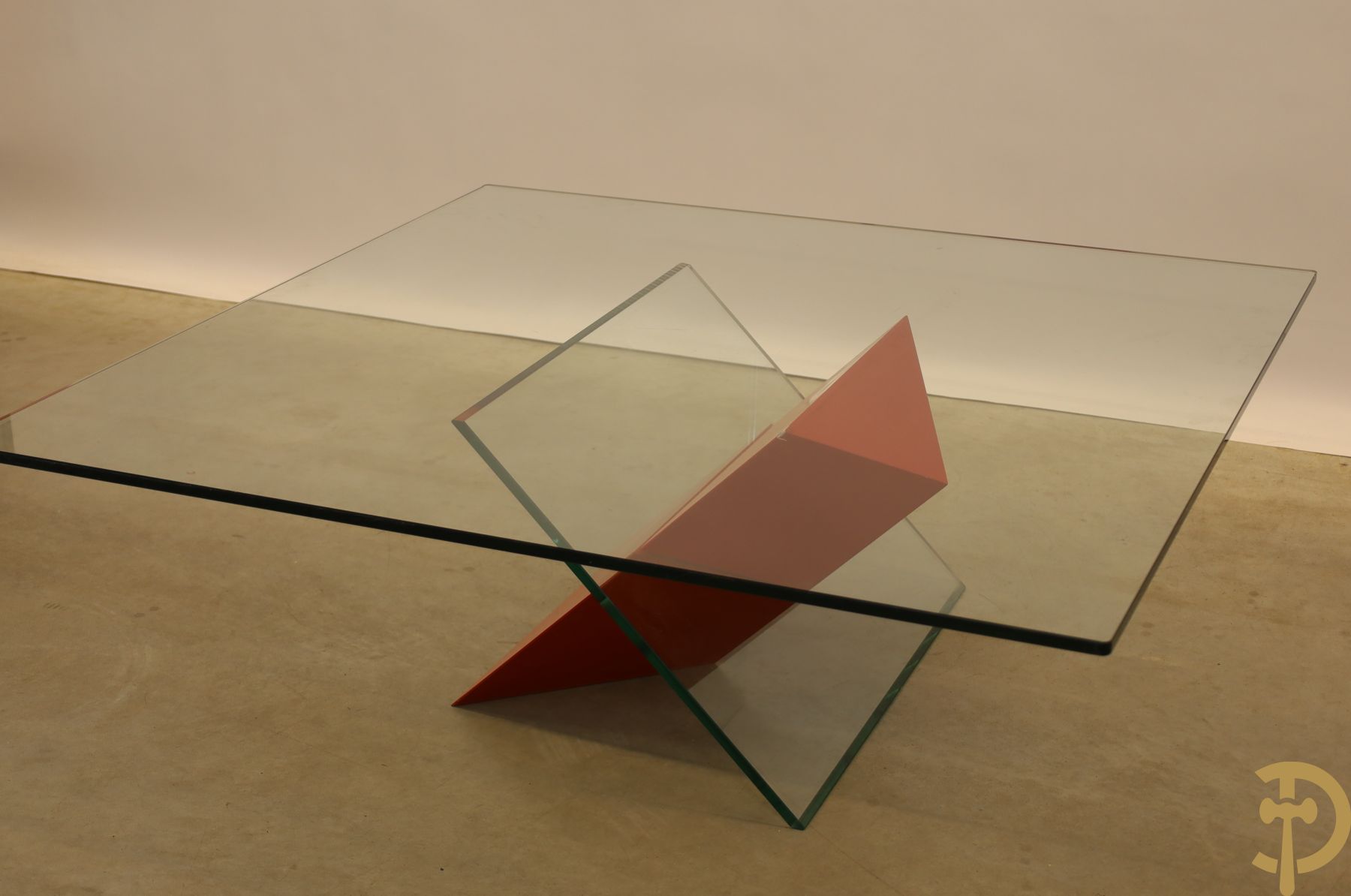 Design salontafel met glazen gepolijst blad op rood gelakte driehoekig prisma sokkel