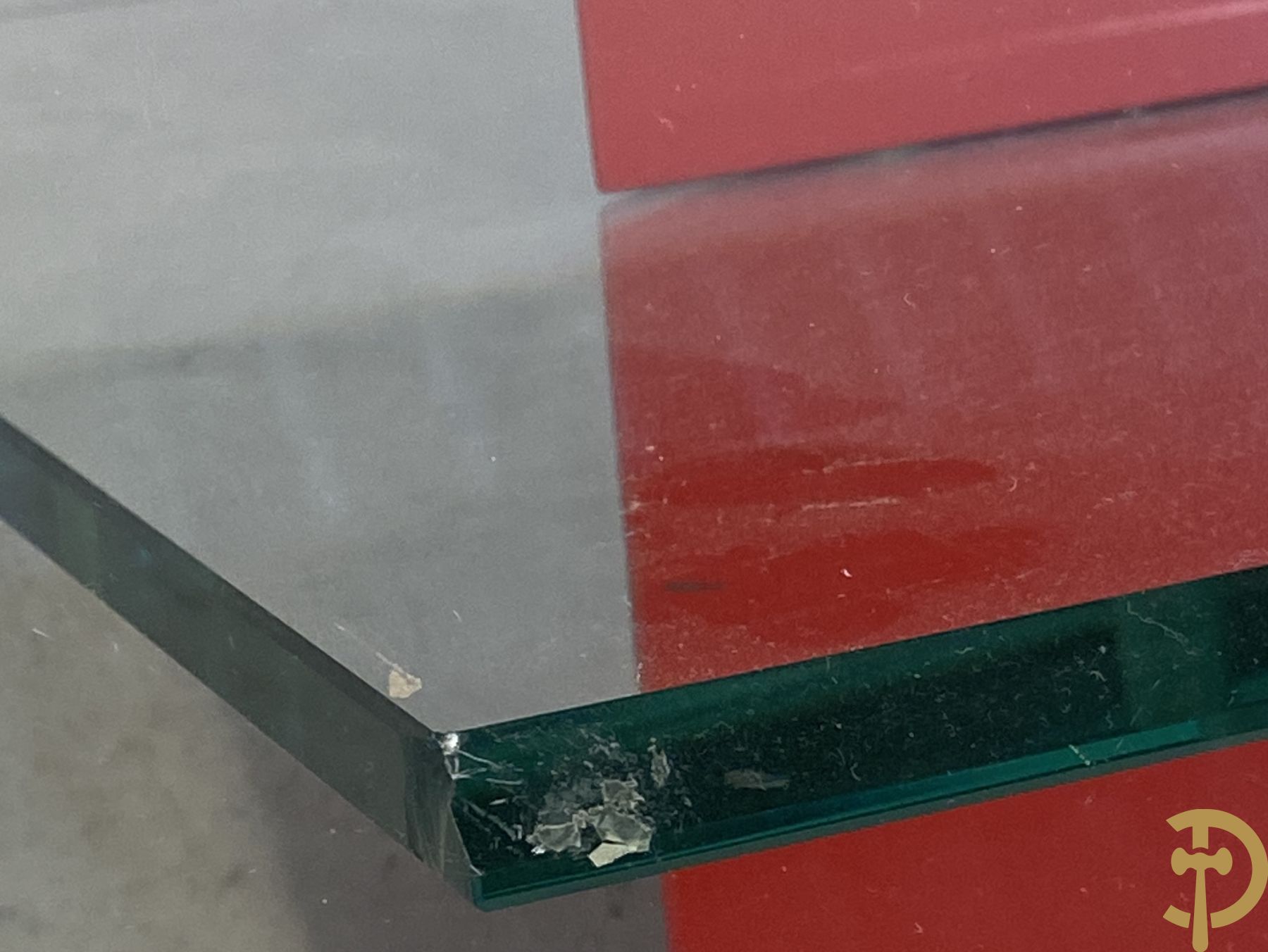 Design salontafel met glazen gepolijst blad op rood gelakte driehoekig prisma sokkel