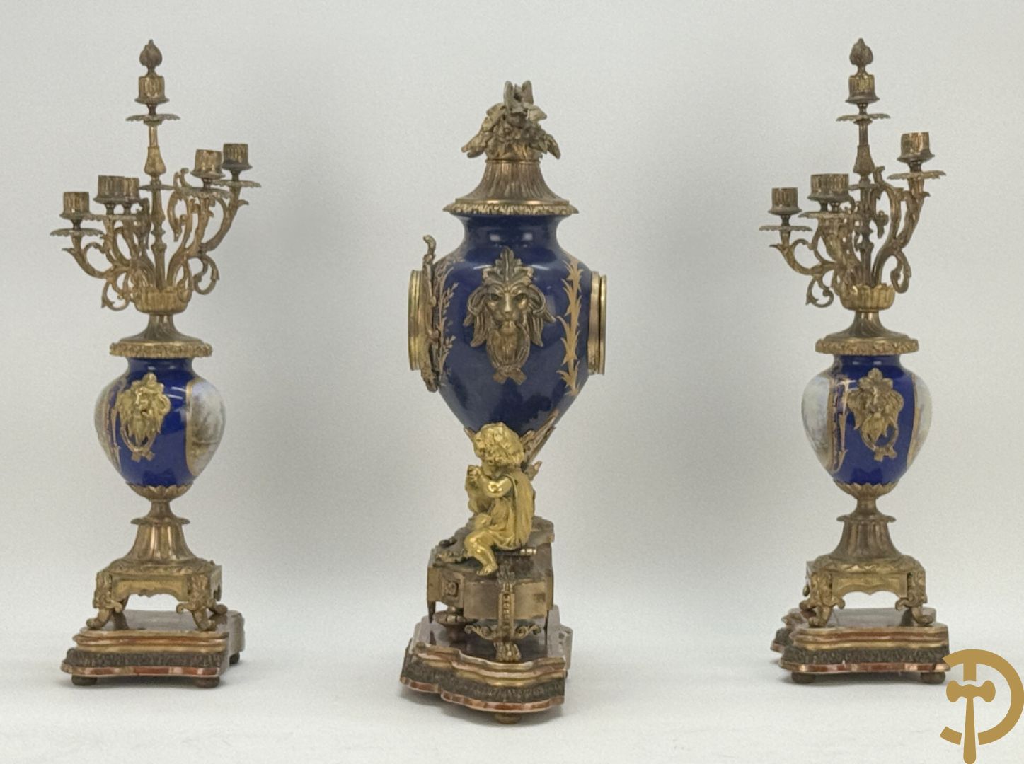 Driedelige vergulde bronzen garnituur bestaande uit pendule met blauw porseleinen coupe geflankeerd door 2 cupido
