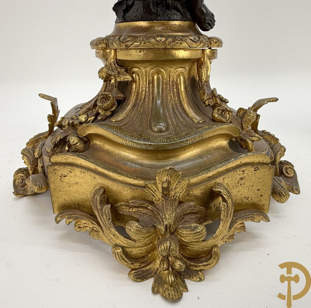 Driedelige bronzen garnituur bestaande uit middenstuk met bronzen vuurvergulde klok, Daubrée gemerkt à Nancy, bovenaan bekroond met Cleopatra met drinkbeker - getekend van Cumberworth sculpteur - geflankeerd door paar cupido