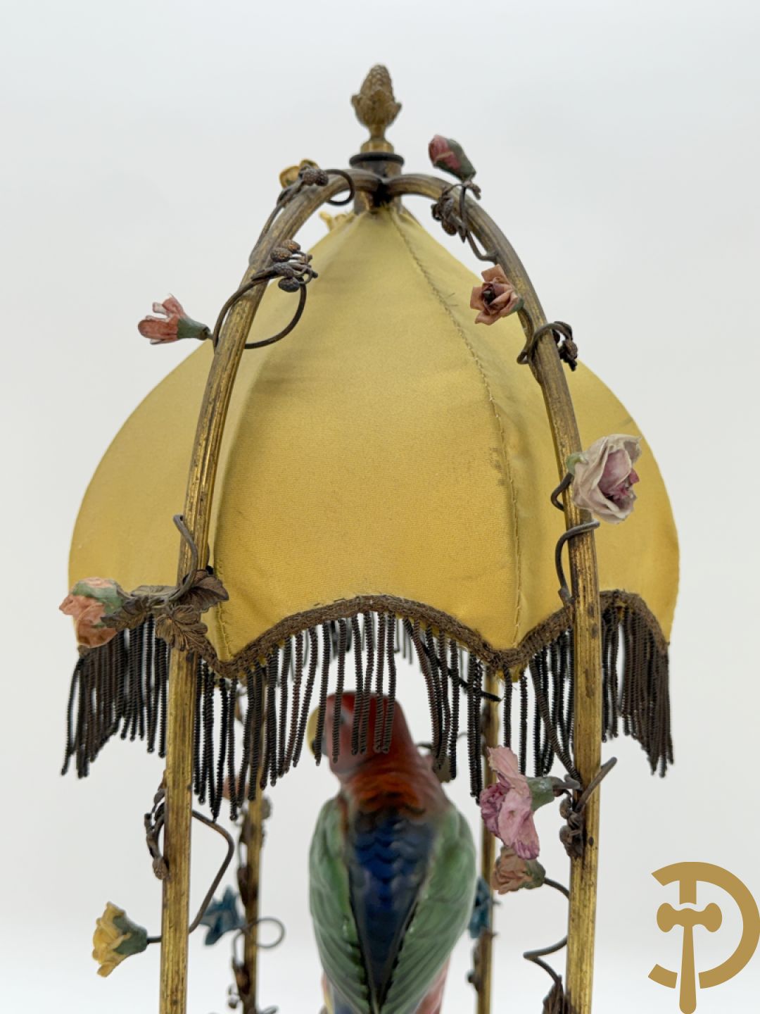 Handgekleurde porseleinen papegaai onder koperen boog met bloemen bezet, als lampadaire