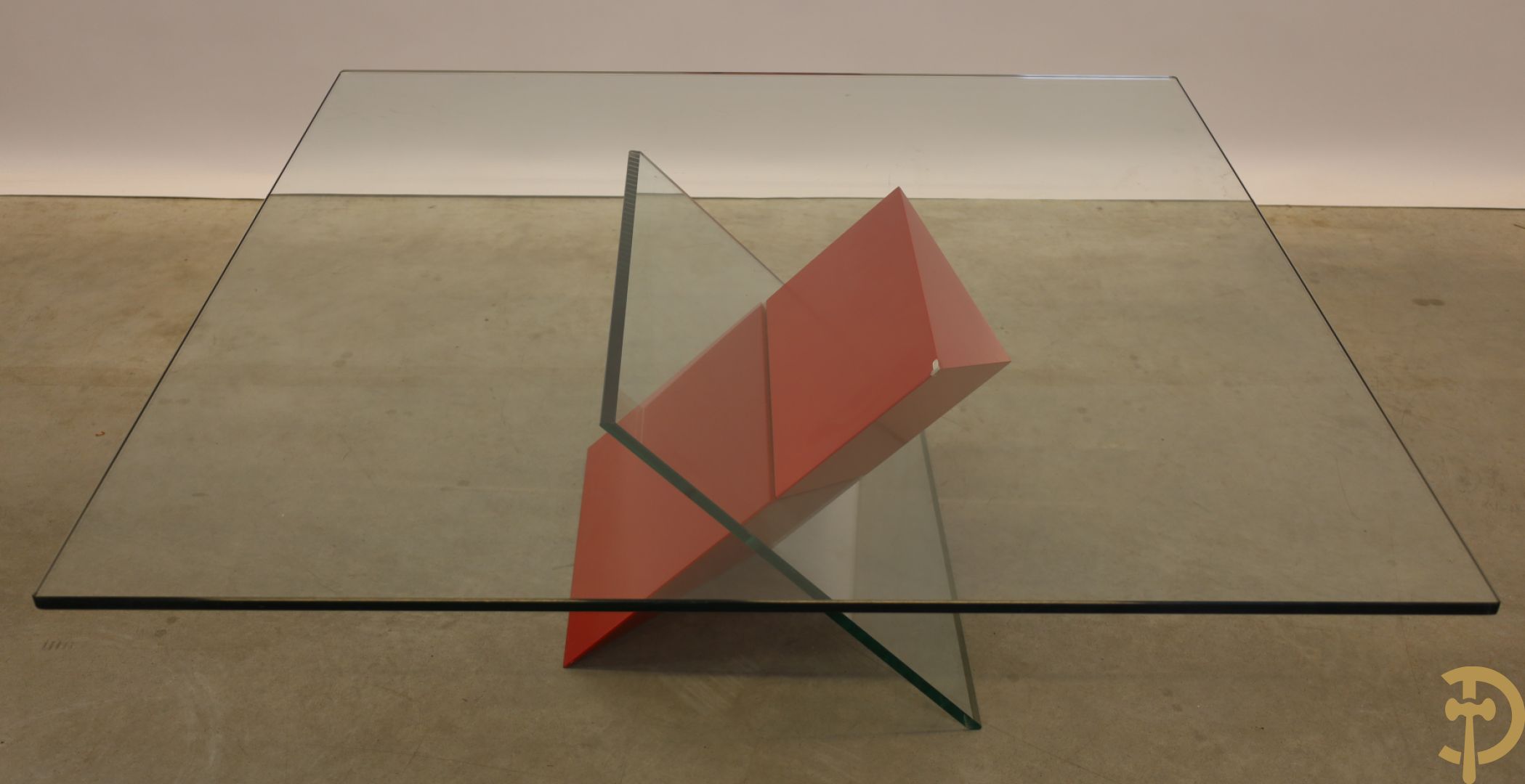 Design salontafel met glazen gepolijst blad op rood gelakte driehoekig prisma sokkel