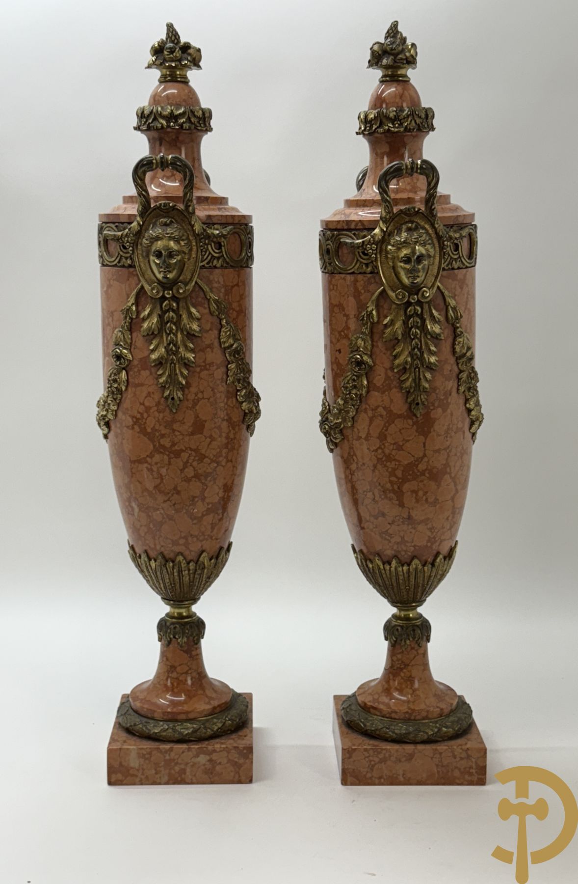 Paar oranje/rode marmeren cassolettes, zijdelings bezet met dameshoofden dragende een guirlande van bloemen - bovenaan met bloementroffee