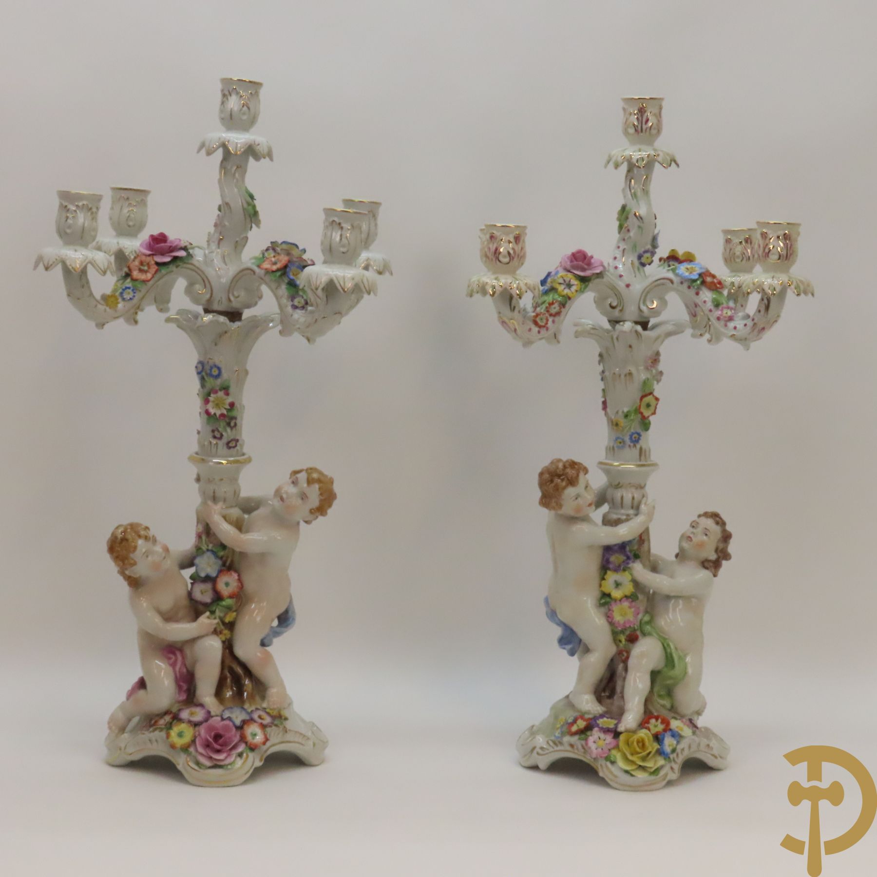 Twee porseleinen vijfarmige kandelaars met cupido's en bezet met bloemen