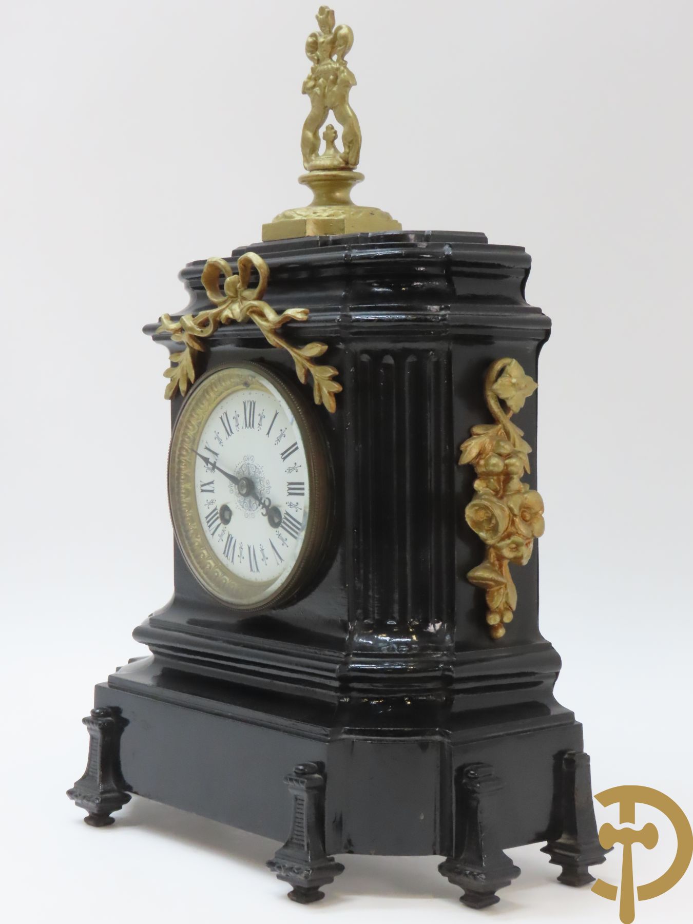 Gepatineerde gietijzeren pendule met bloemenmotieven en Louis XVI strik, bovenaan bekroond met ornament