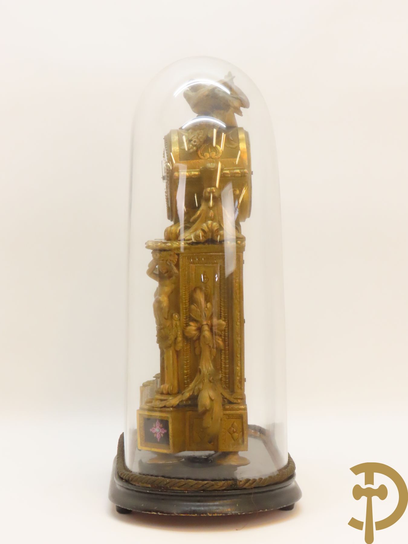 Vergulde pendule in zamak, wijzerplaat bezet met porseleinen plakkettes - bovenaan met vogelpaar, zijdelings met kariathyden houdende een bloementroffee - onder glazen stolp