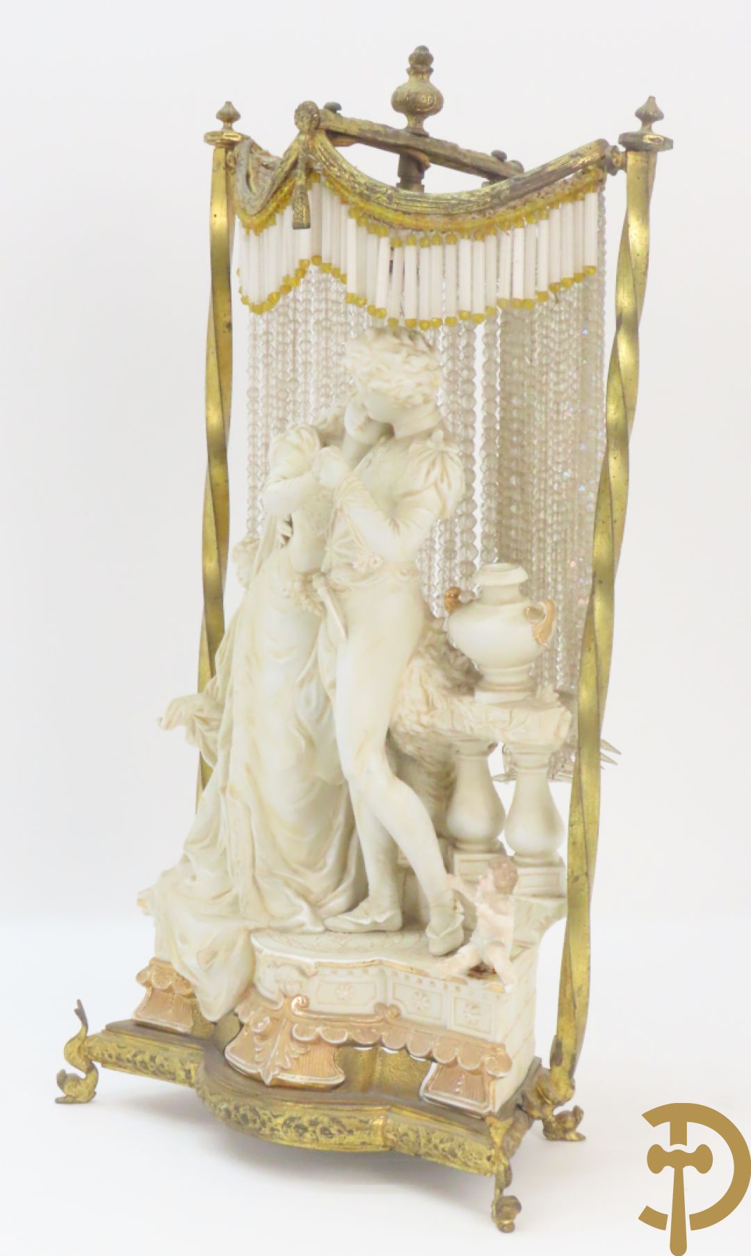 Lieftallig biscuit van romantisch koppel bij amfoor met kleine neergezeten cupido onder koperen baldakijn met kristallen belletjes