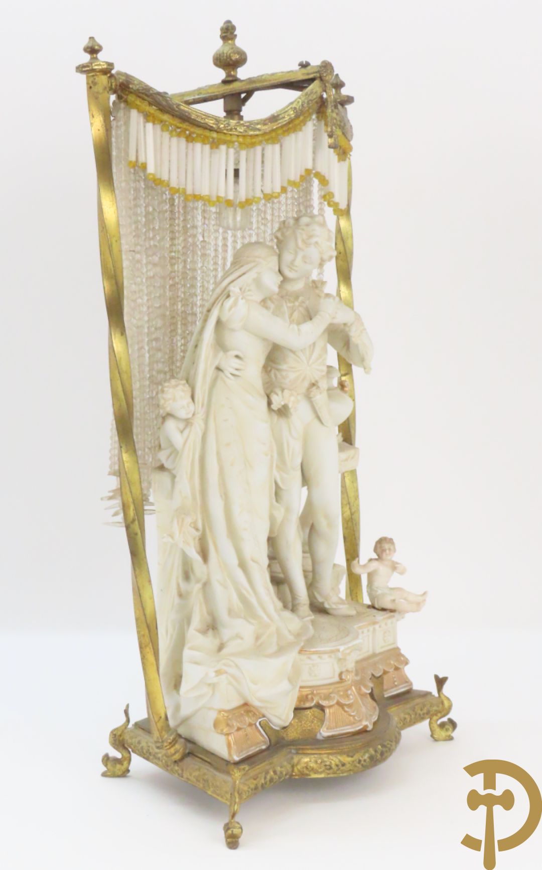 Lieftallig biscuit van romantisch koppel bij amfoor met kleine neergezeten cupido onder koperen baldakijn met kristallen belletjes