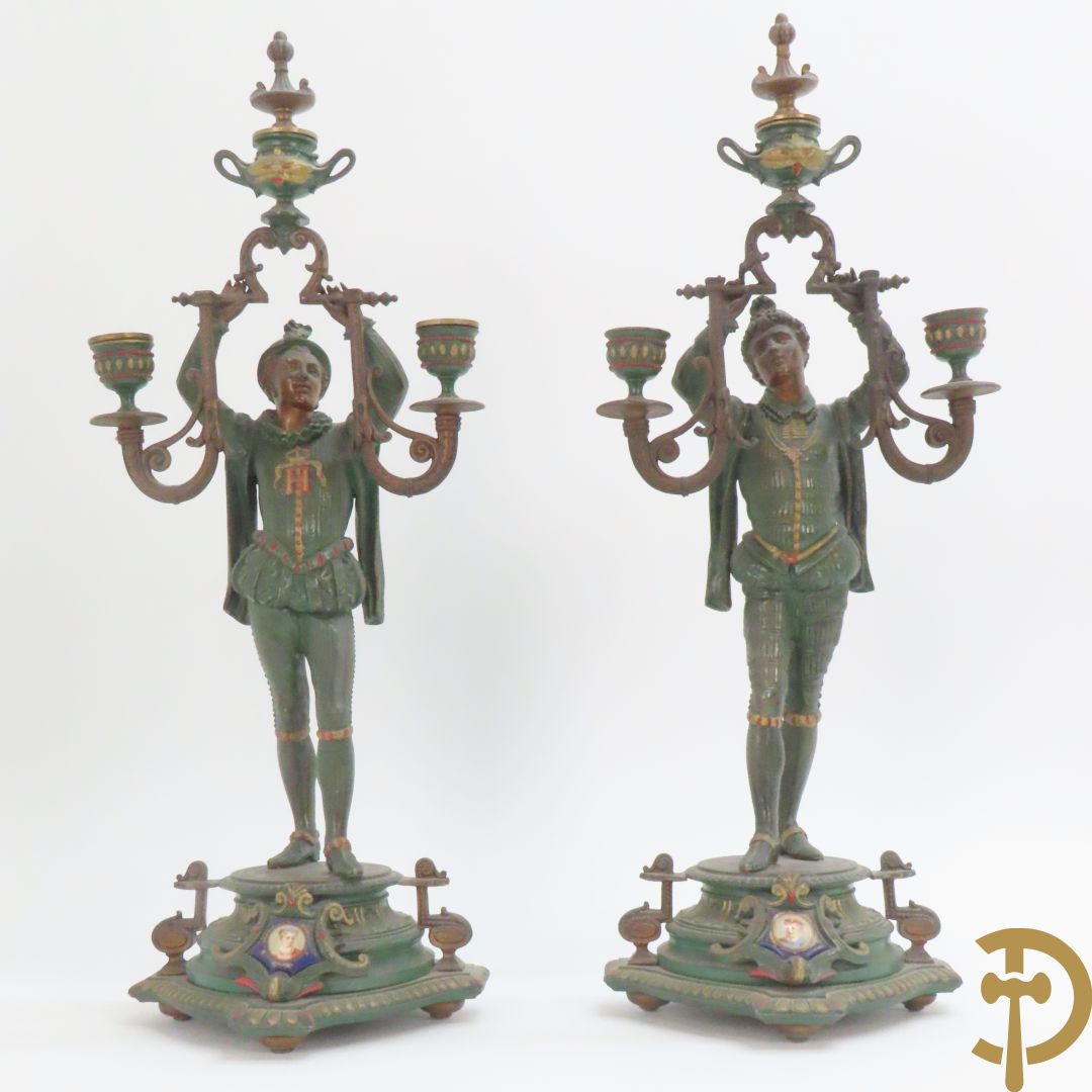 Driedelige kunstbronzen garnituur bestaande uit pendule met paar schakende edelheren, bezet met kariatiden - geflankeerd door paar driearmige kandelaars gehouden door 2 edelheren