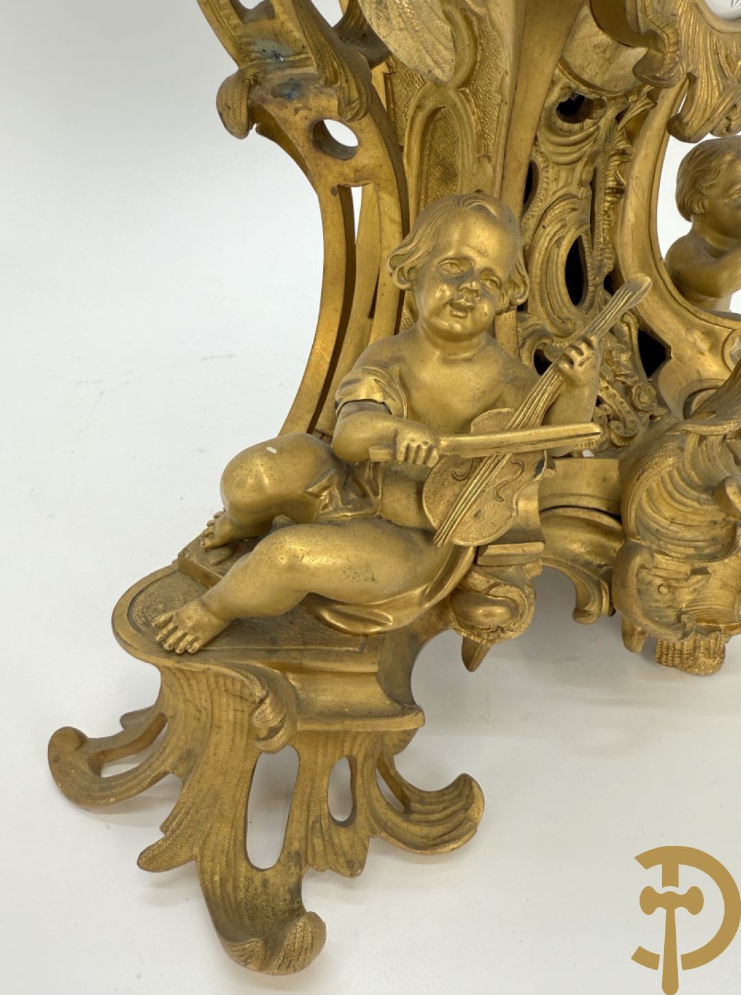 Driedelige vuurvergulde bronzen garnituur, Louis XV stijl, bestaande uit middenstuk met klok omgeven door musicerende cupido