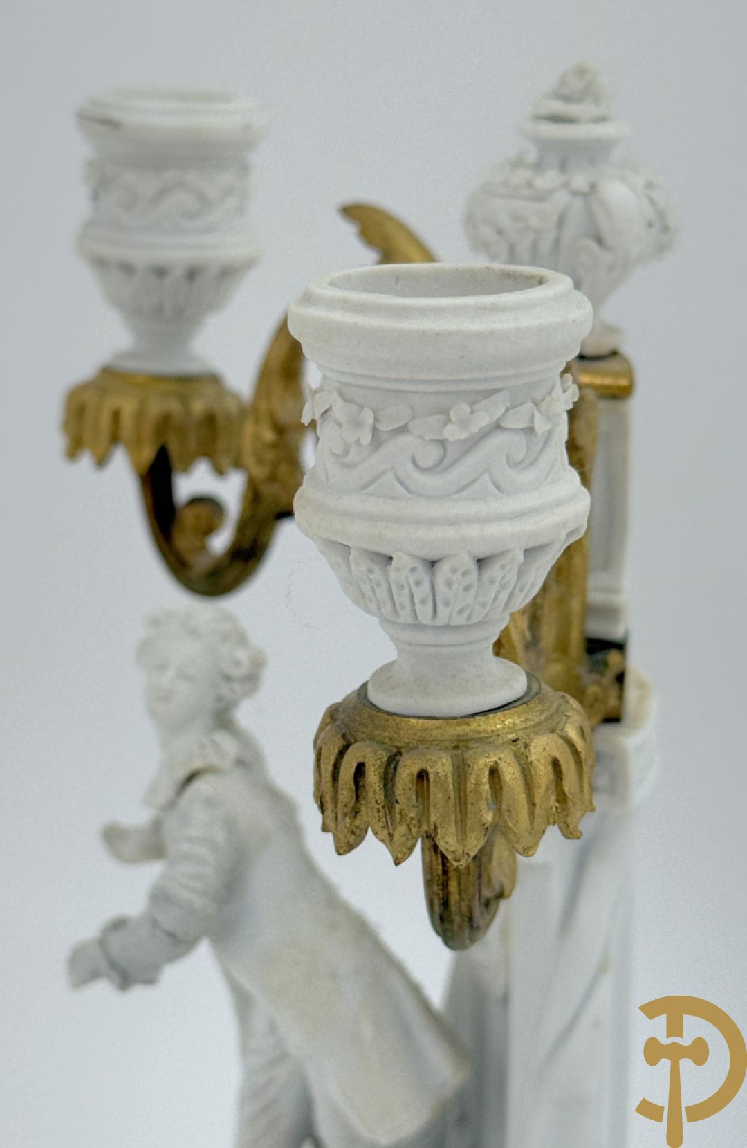 Driedelige porseleinen garnituur met bronsbeslag bestaande uit pendule met dame en amfoor geflankeerd door paar kandelaars bezet met personages