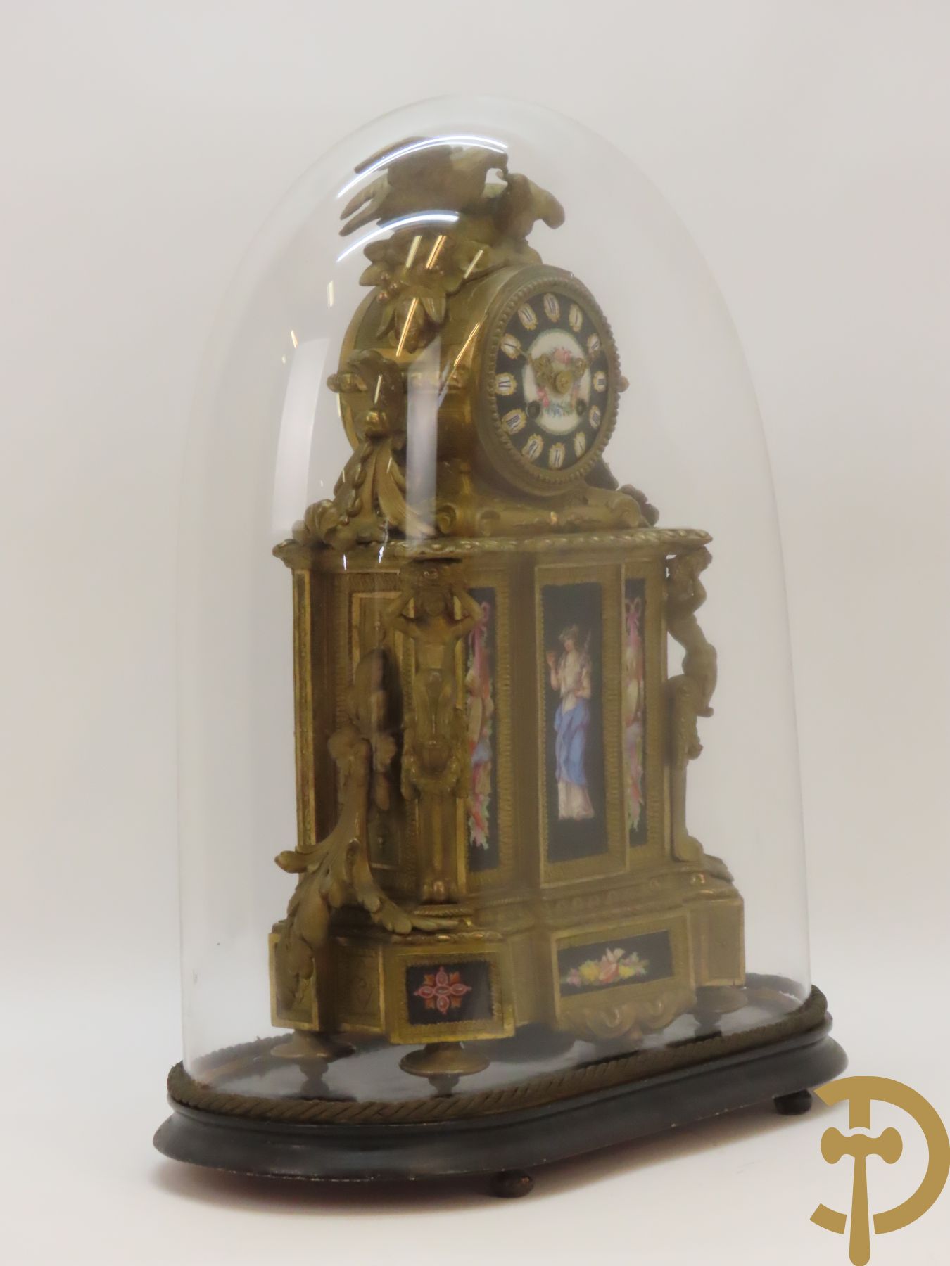 Vergulde pendule in zamak, wijzerplaat bezet met porseleinen plakkettes - bovenaan met vogelpaar, zijdelings met kariathyden houdende een bloementroffee - onder glazen stolp