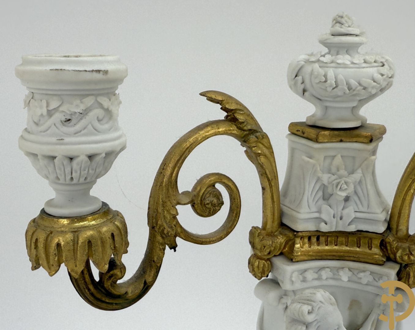 Driedelige porseleinen garnituur met bronsbeslag bestaande uit pendule met dame en amfoor geflankeerd door paar kandelaars bezet met personages