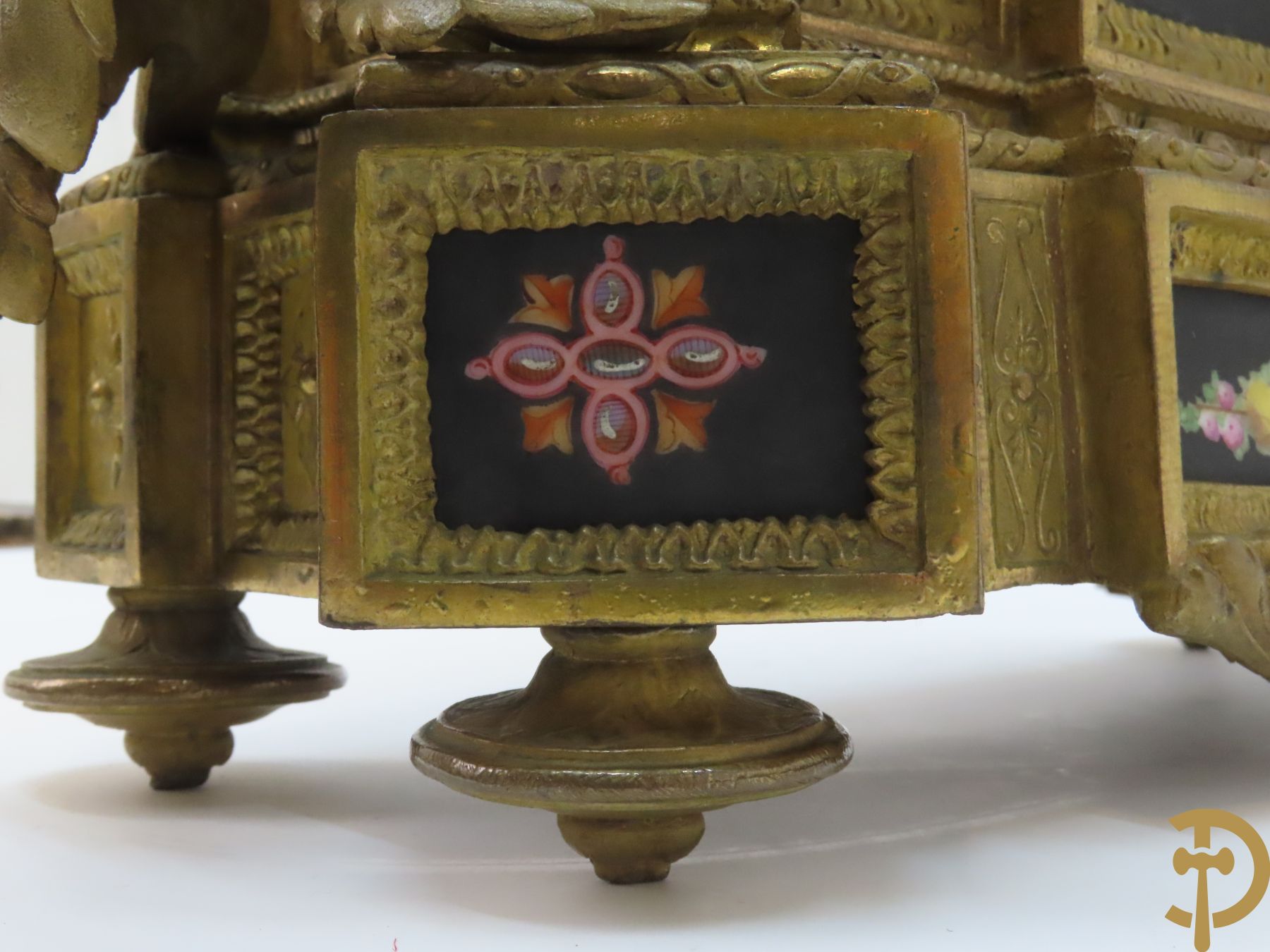 Vergulde pendule in zamak, wijzerplaat bezet met porseleinen plakkettes - bovenaan met vogelpaar, zijdelings met kariathyden houdende een bloementroffee - onder glazen stolp