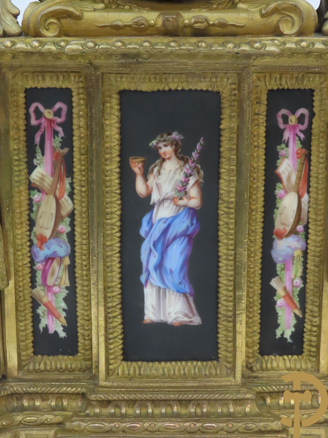 Vergulde pendule in zamak, wijzerplaat bezet met porseleinen plakkettes - bovenaan met vogelpaar, zijdelings met kariathyden houdende een bloementroffee - onder glazen stolp