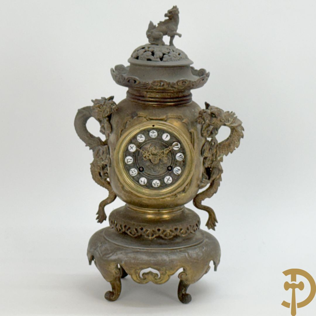 Aziatische pendule in zamak, zijdelings bezet met drakendecor en bovenaan met mythologisch figuur