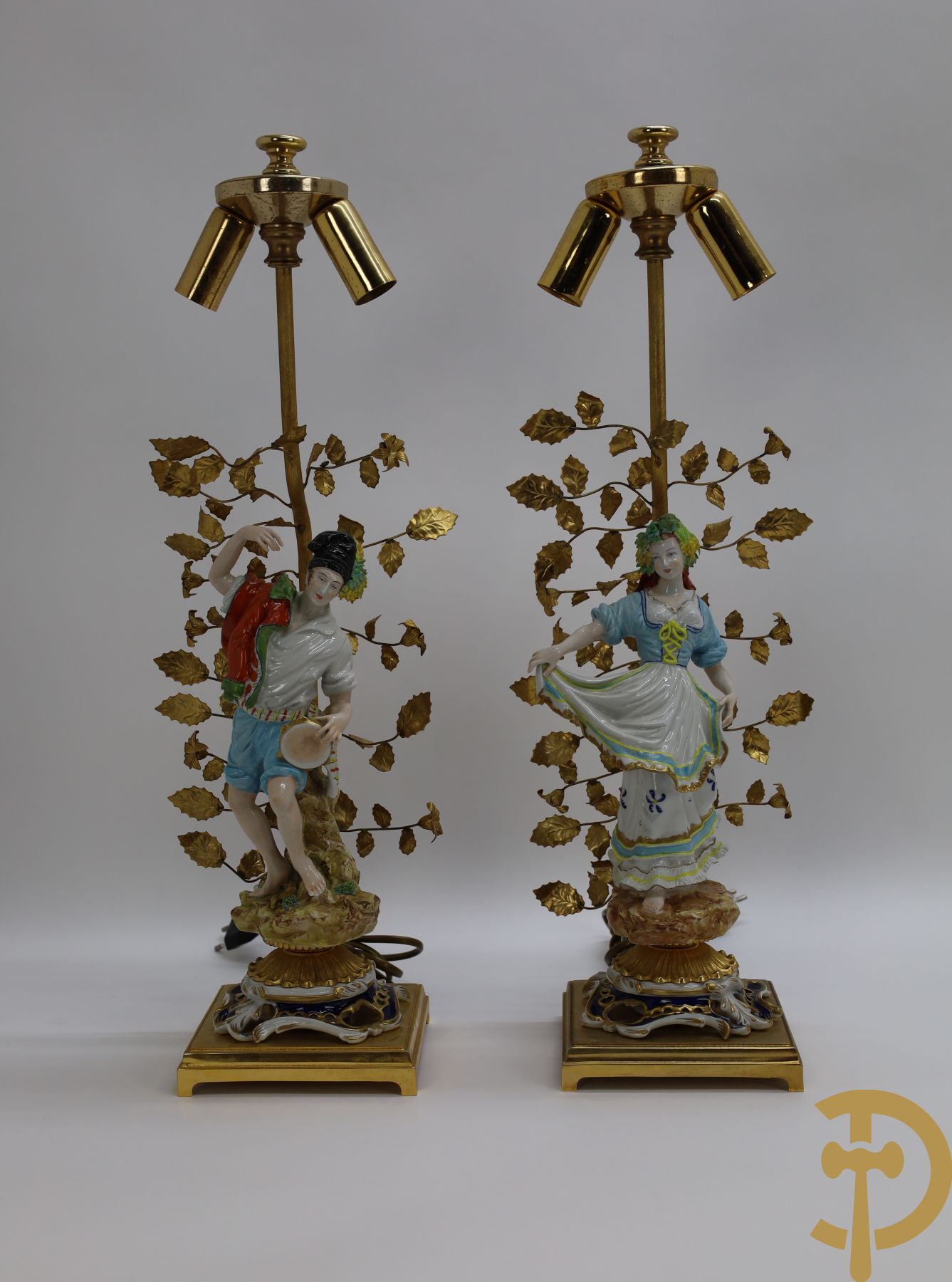 Paar koperen lampadaires met bladranken bezet met porseleinen beeld van dame met hoepeljurk en heer met tamboer