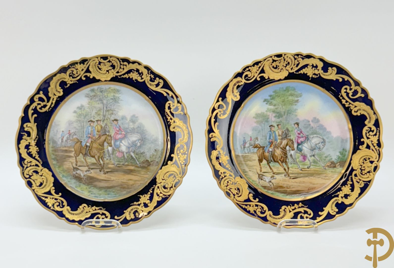 Paar porseleinen borden met ruitertafereel met vergulde omranding, getekend Rivière en Bourdier P., achteraan gemerkt met gekruiste pijlen