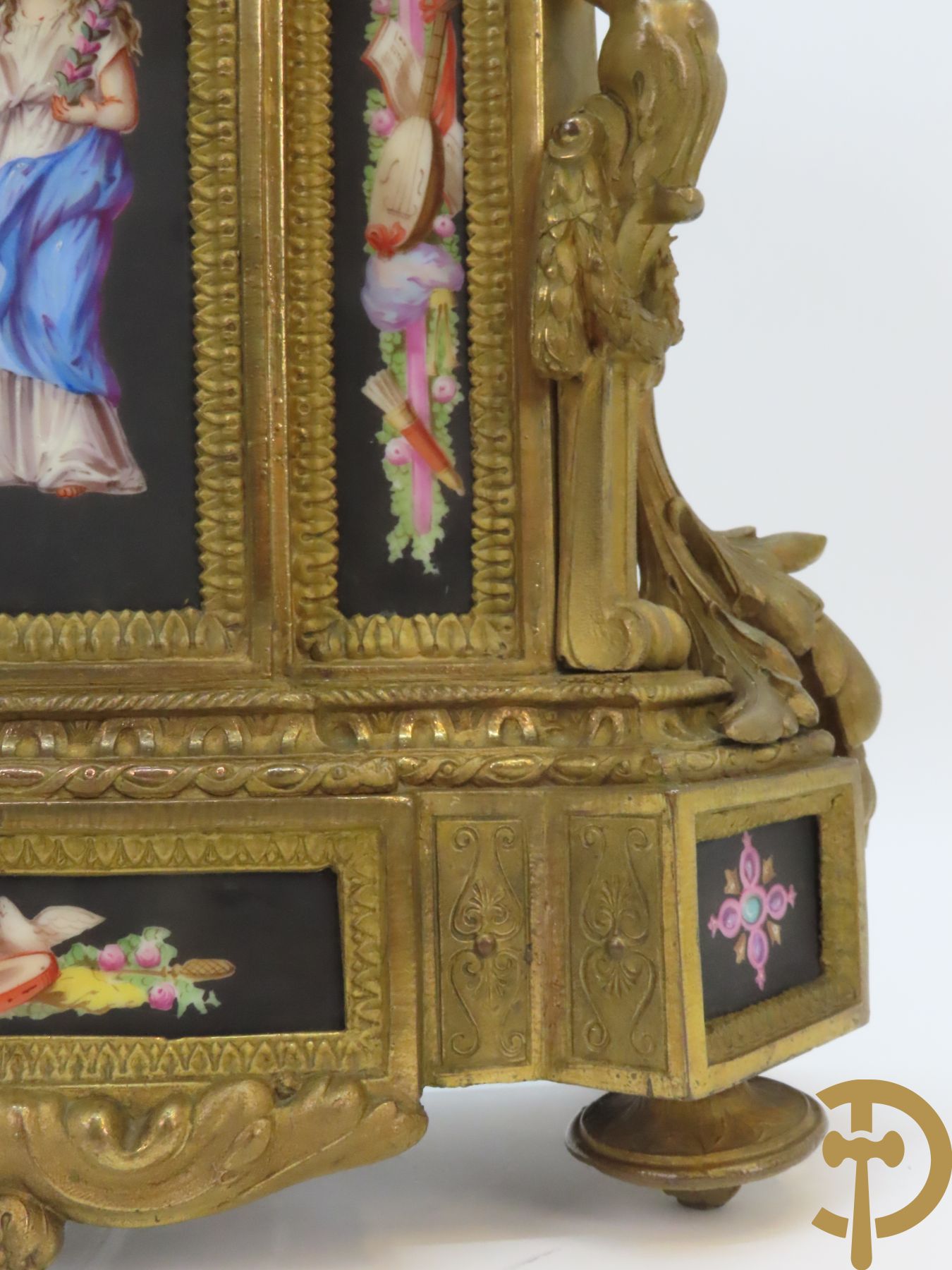 Vergulde pendule in zamak, wijzerplaat bezet met porseleinen plakkettes - bovenaan met vogelpaar, zijdelings met kariathyden houdende een bloementroffee - onder glazen stolp