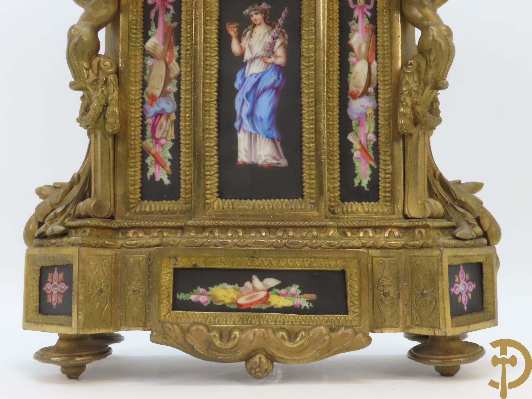 Vergulde pendule in zamak, wijzerplaat bezet met porseleinen plakkettes - bovenaan met vogelpaar, zijdelings met kariathyden houdende een bloementroffee - onder glazen stolp