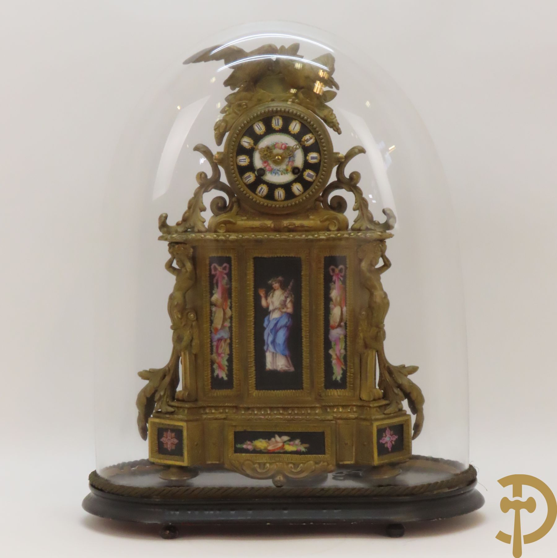 Vergulde pendule in zamak, wijzerplaat bezet met porseleinen plakkettes - bovenaan met vogelpaar, zijdelings met kariathyden houdende een bloementroffee - onder glazen stolp