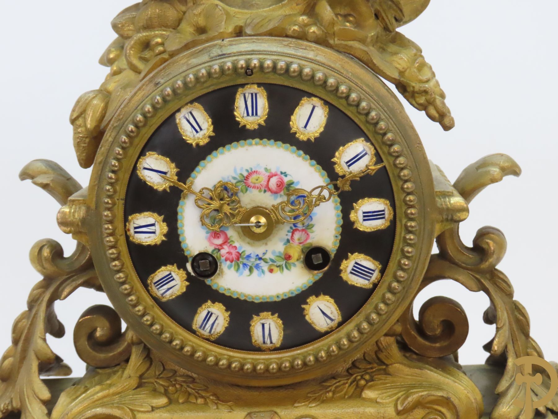 Vergulde pendule in zamak, wijzerplaat bezet met porseleinen plakkettes - bovenaan met vogelpaar, zijdelings met kariathyden houdende een bloementroffee - onder glazen stolp