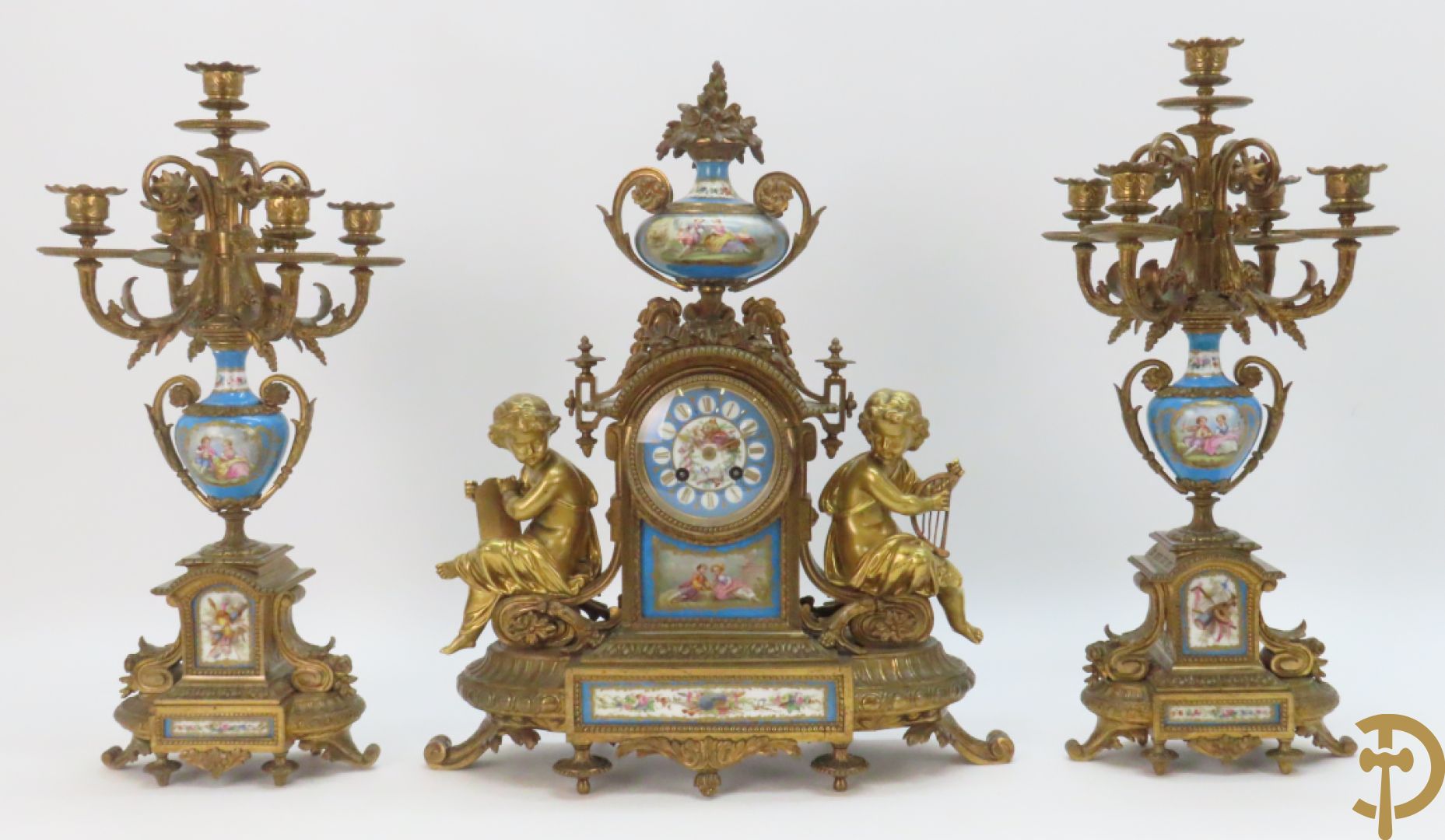 Driedelige bronzen garnituur bezet met Sèvres porselein bestaande uit pendule geflankeerd door paar cupido's - bovenaan met amfoor in Sèvres porselein met romantisch decor + paar bronzen zijstukken met vijf kaarsenhouders - centraal met porseleinen Sèvres amfoorvaasje beschilderd met romantische taferelen, 19e